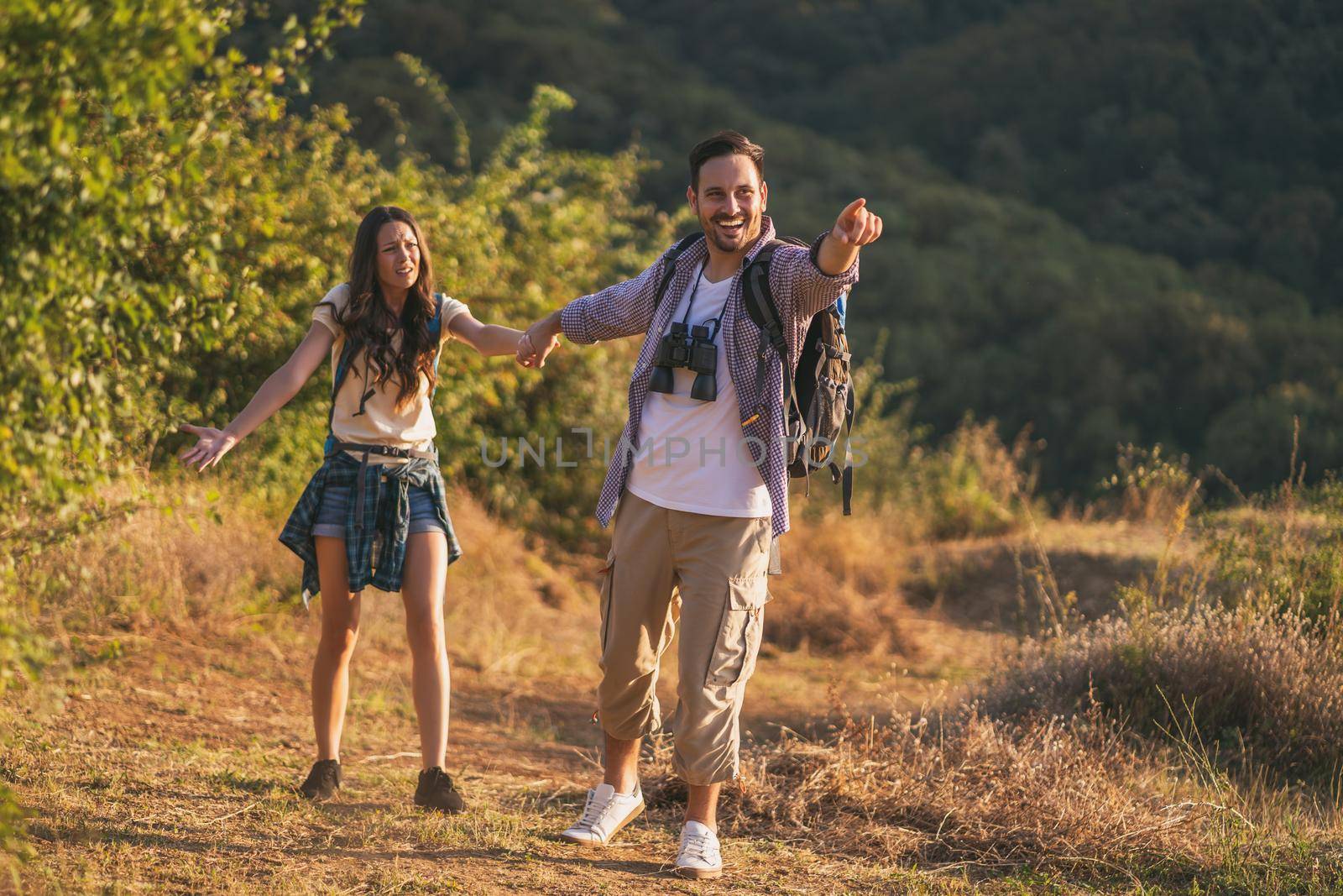 Happy couple is hiking in mountain. Woman is tired and wants a pause.