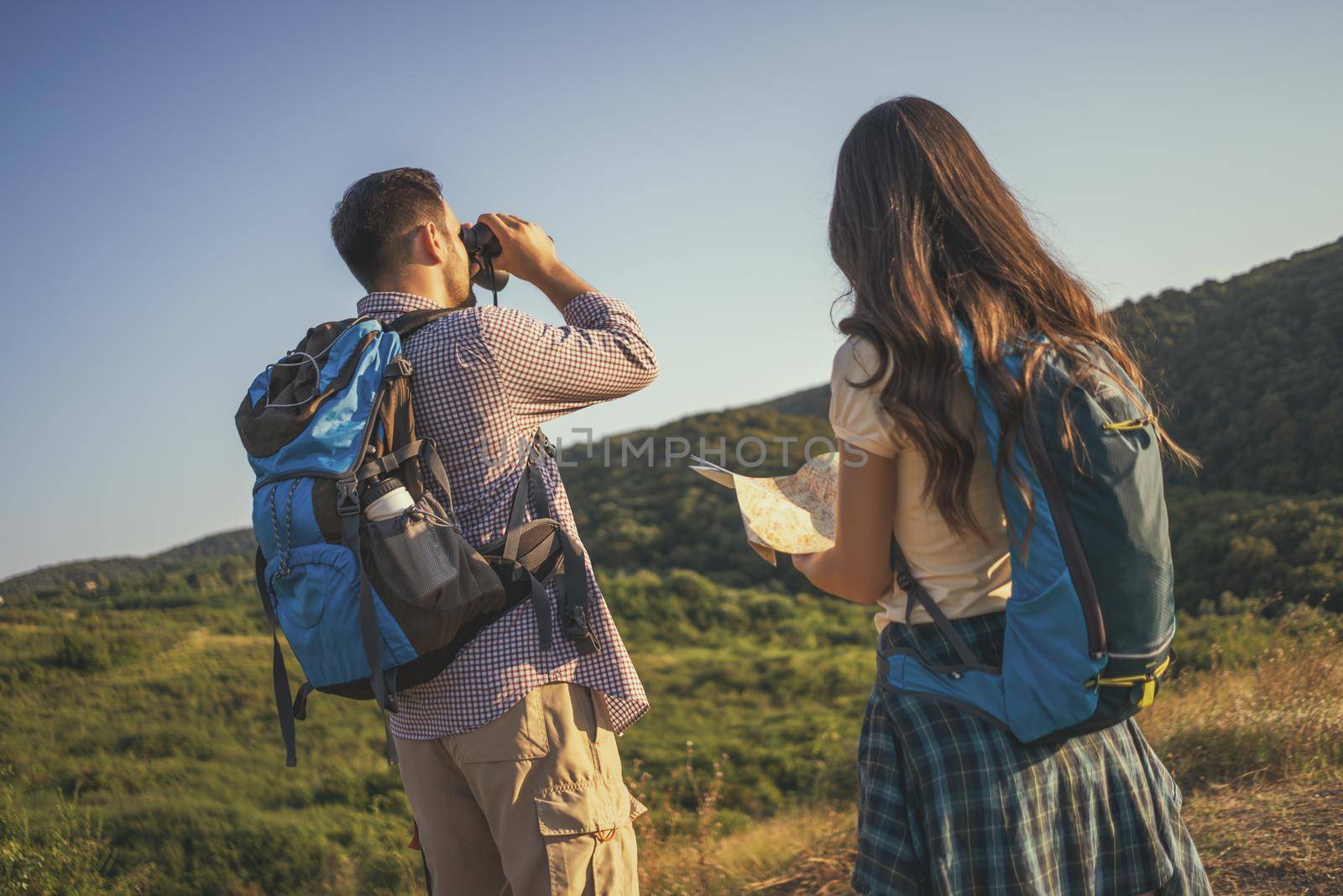 Happy couple is hiking in mountain. They are looking at map.