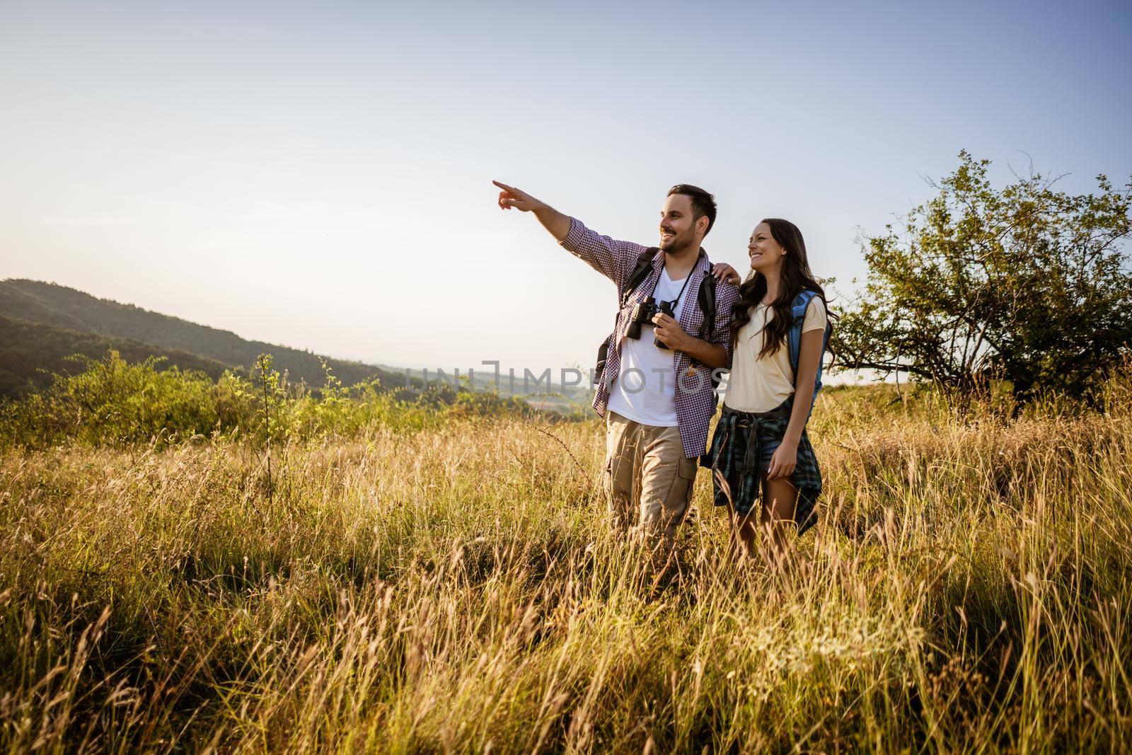 Happy couple is hiking in mountain. They are watching nature with binoculars.