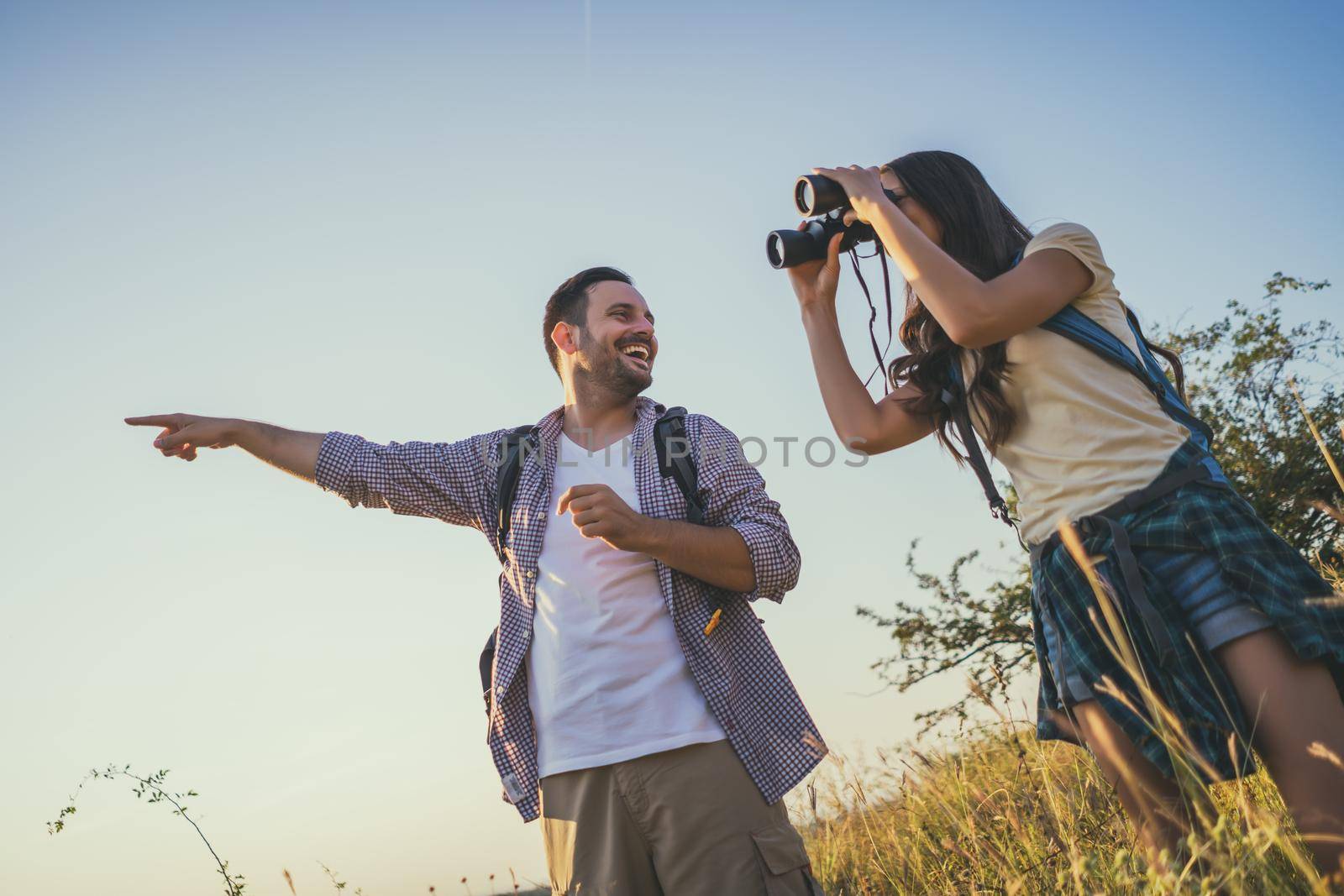 Happy couple is hiking in mountain. They are watching nature with binoculars.