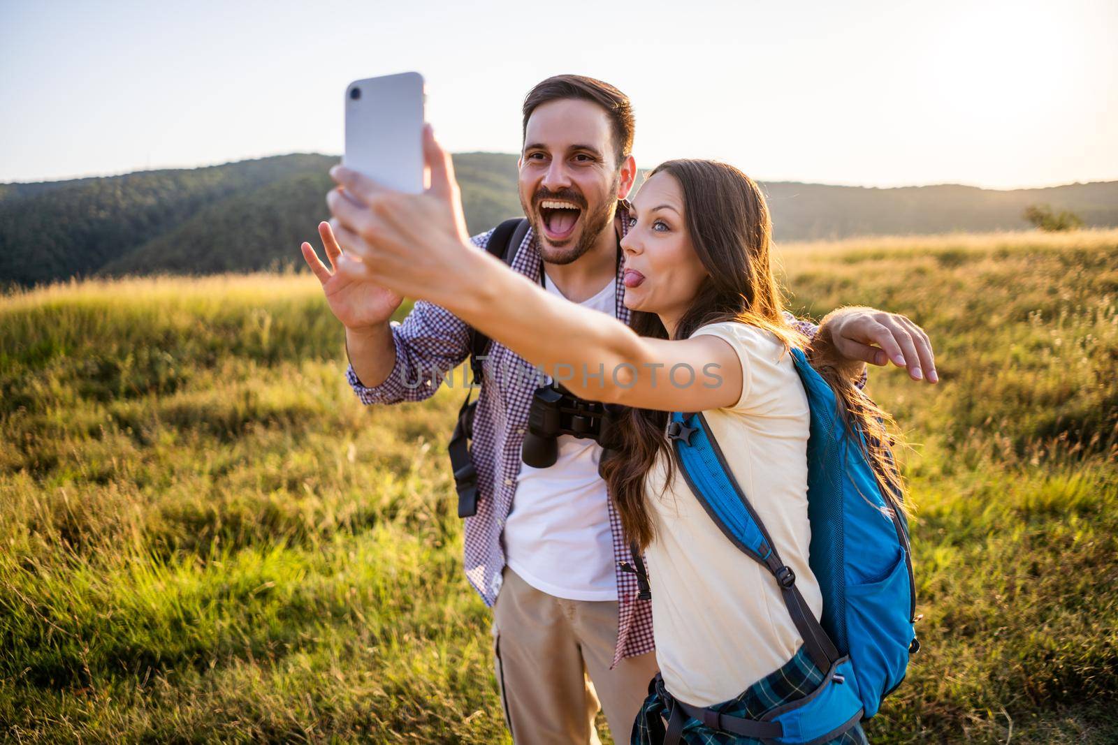 Happy couple is hiking in mountain. They are taking selfie.