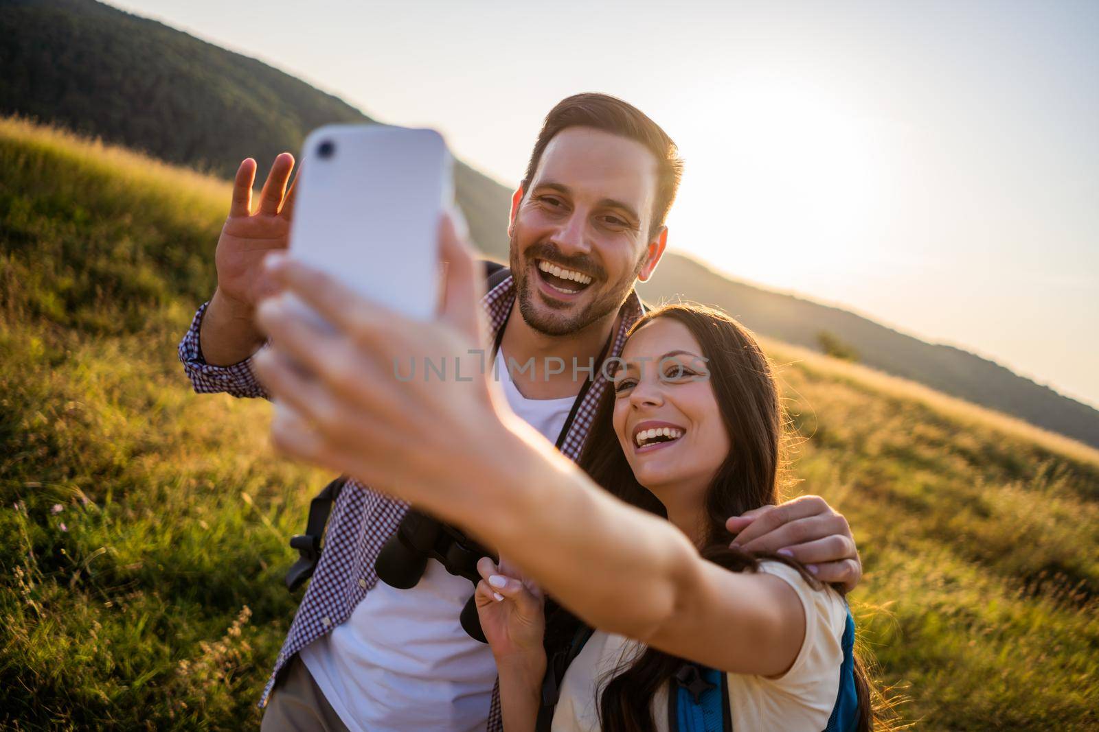 Happy couple is hiking in mountain. They are taking selfie.