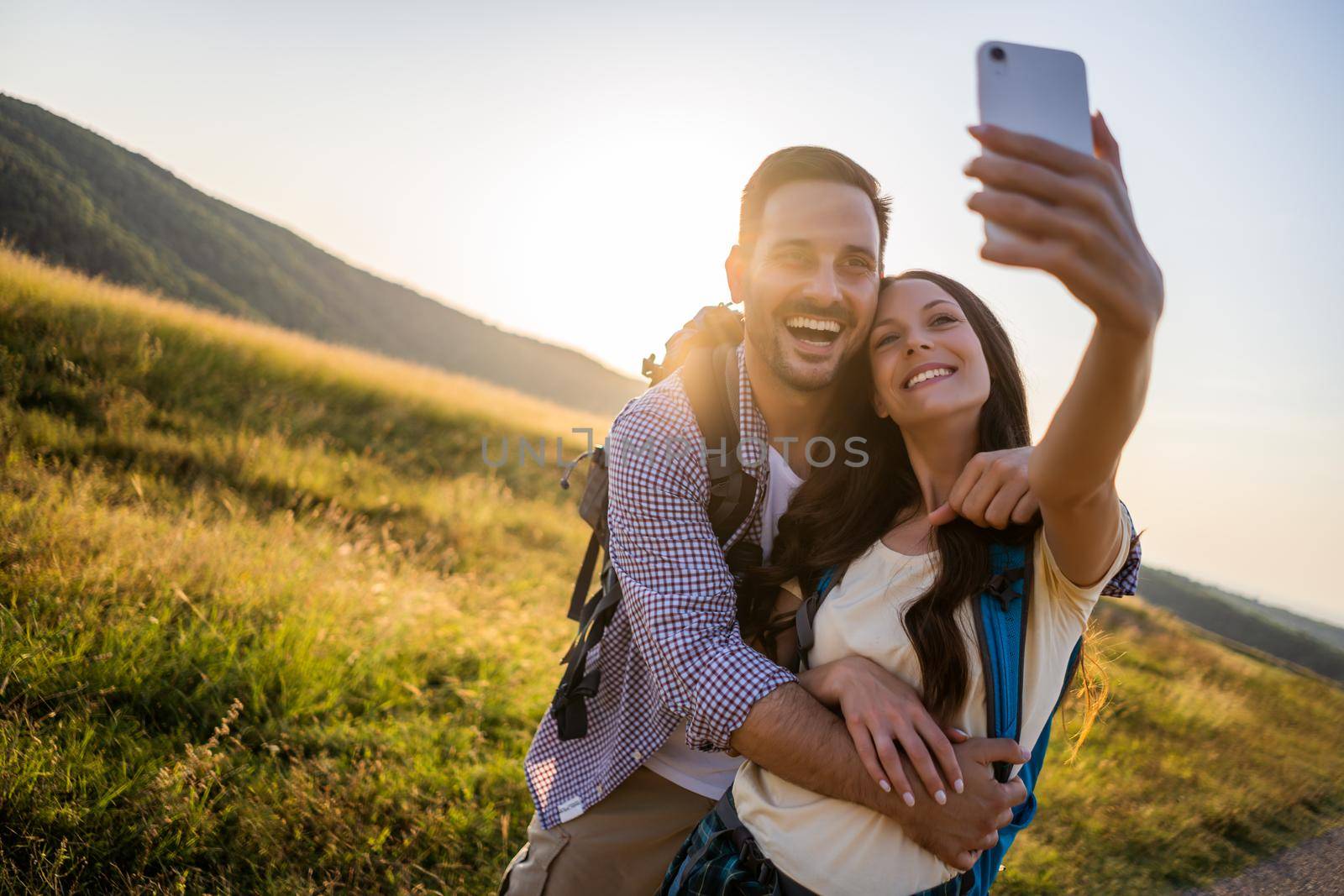 Happy couple is hiking in mountain. They are taking selfie.