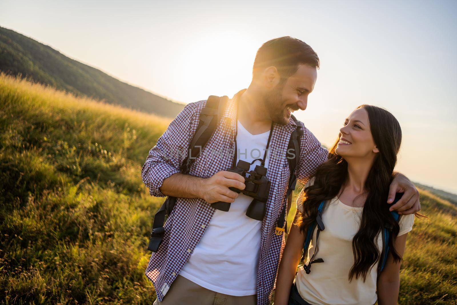 Happy couple is hiking in mountain. They are watching nature with binoculars.