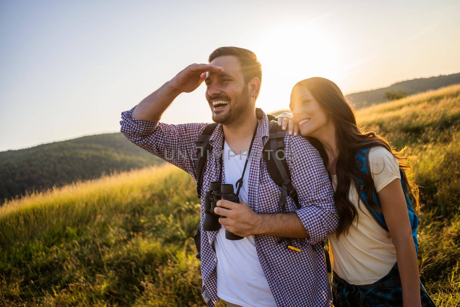 Happy couple is hiking in mountain. They are watching nature with binoculars.