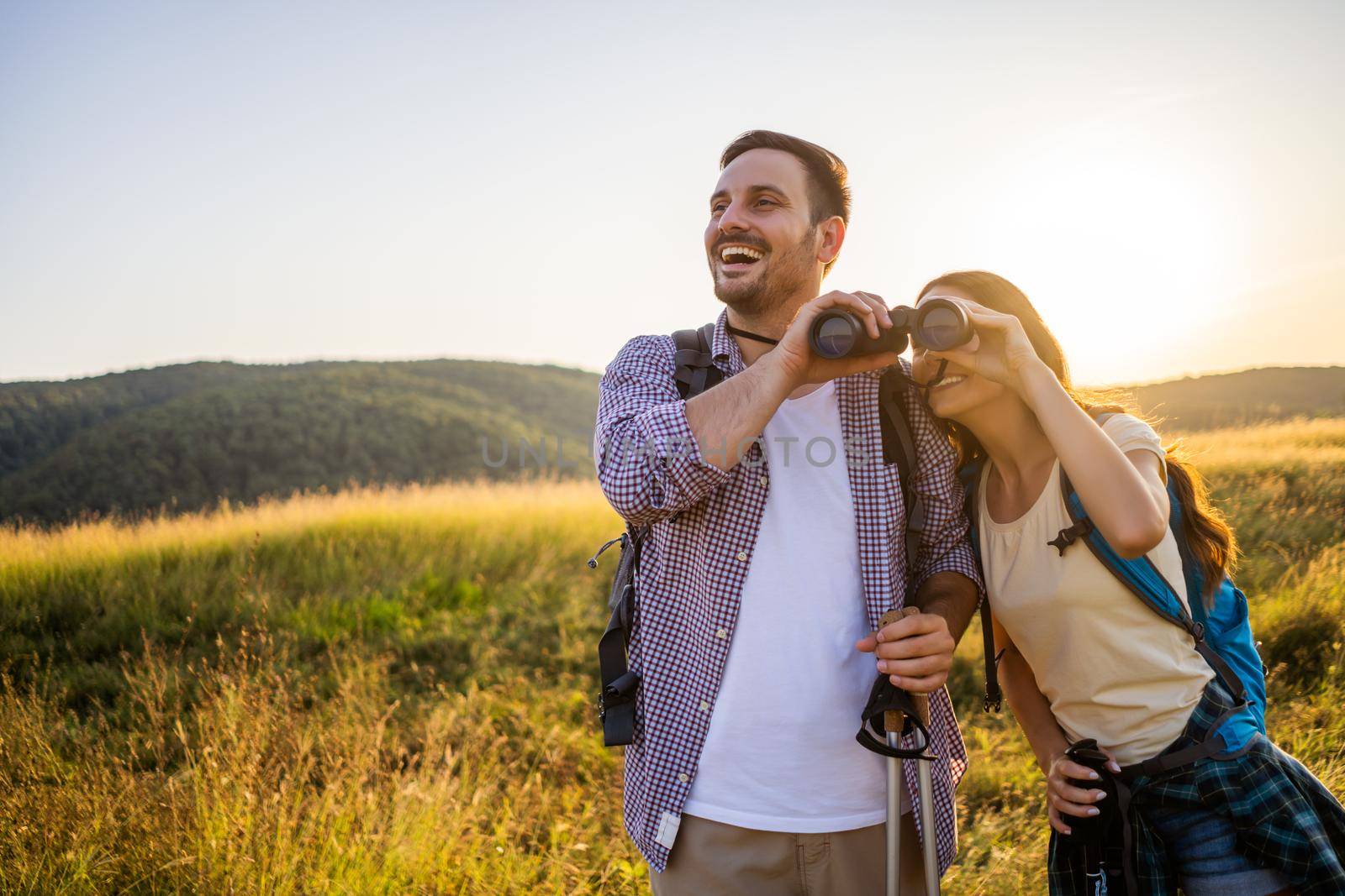 Happy couple is hiking in mountain. They are watching nature with binoculars.