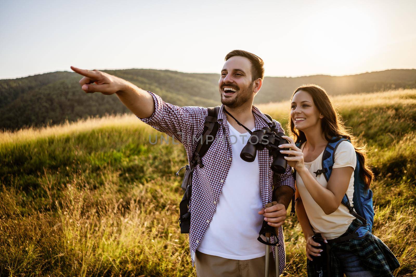 Happy couple is hiking in mountain. They are watching nature with binoculars.