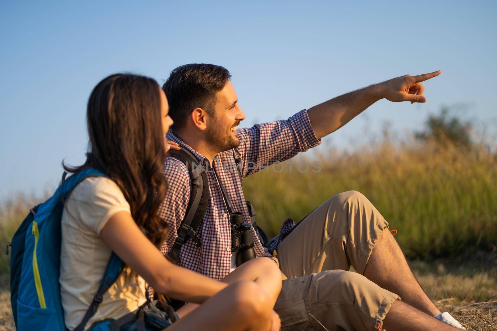 Happy couple is hiking in mountain. They are watching nature with binoculars.