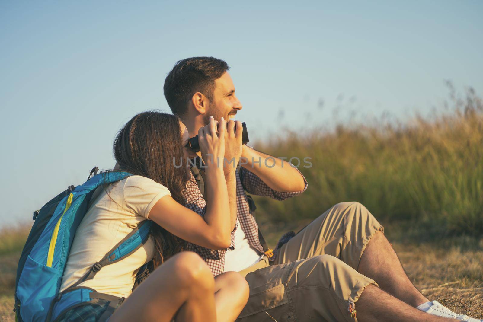 Happy couple is hiking in mountain. They are watching nature with binoculars.