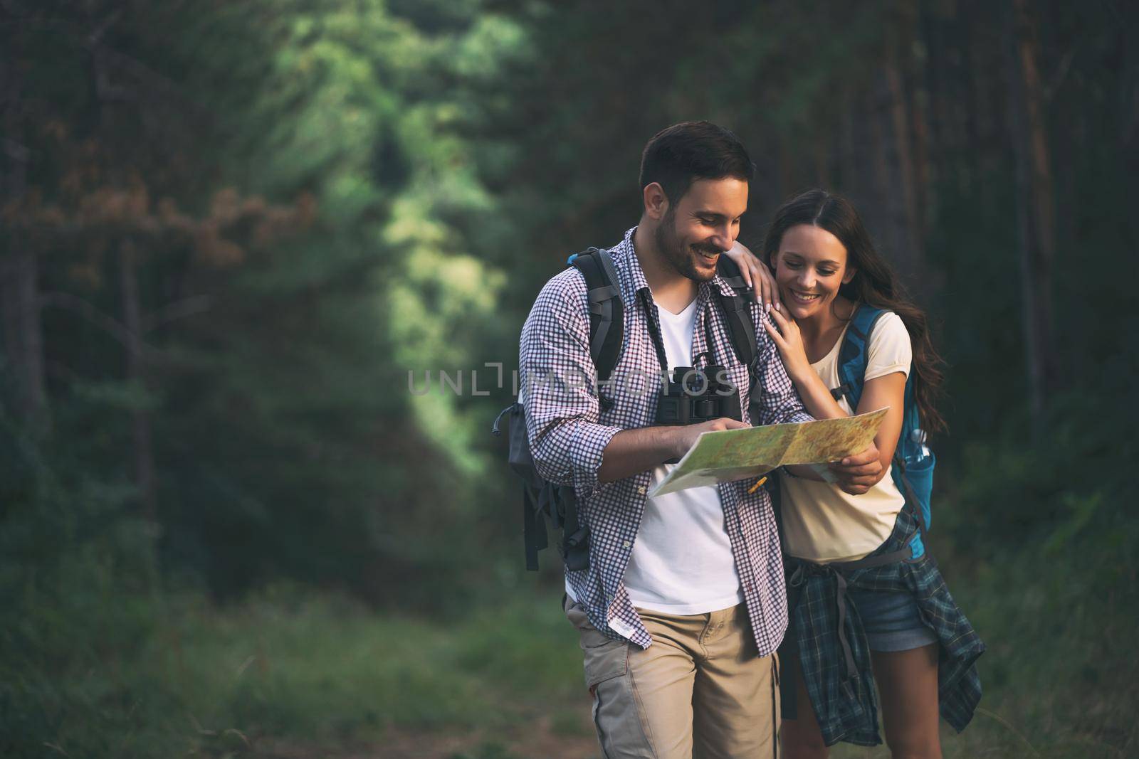 Happy couple is hiking in forest. They are looking at map.