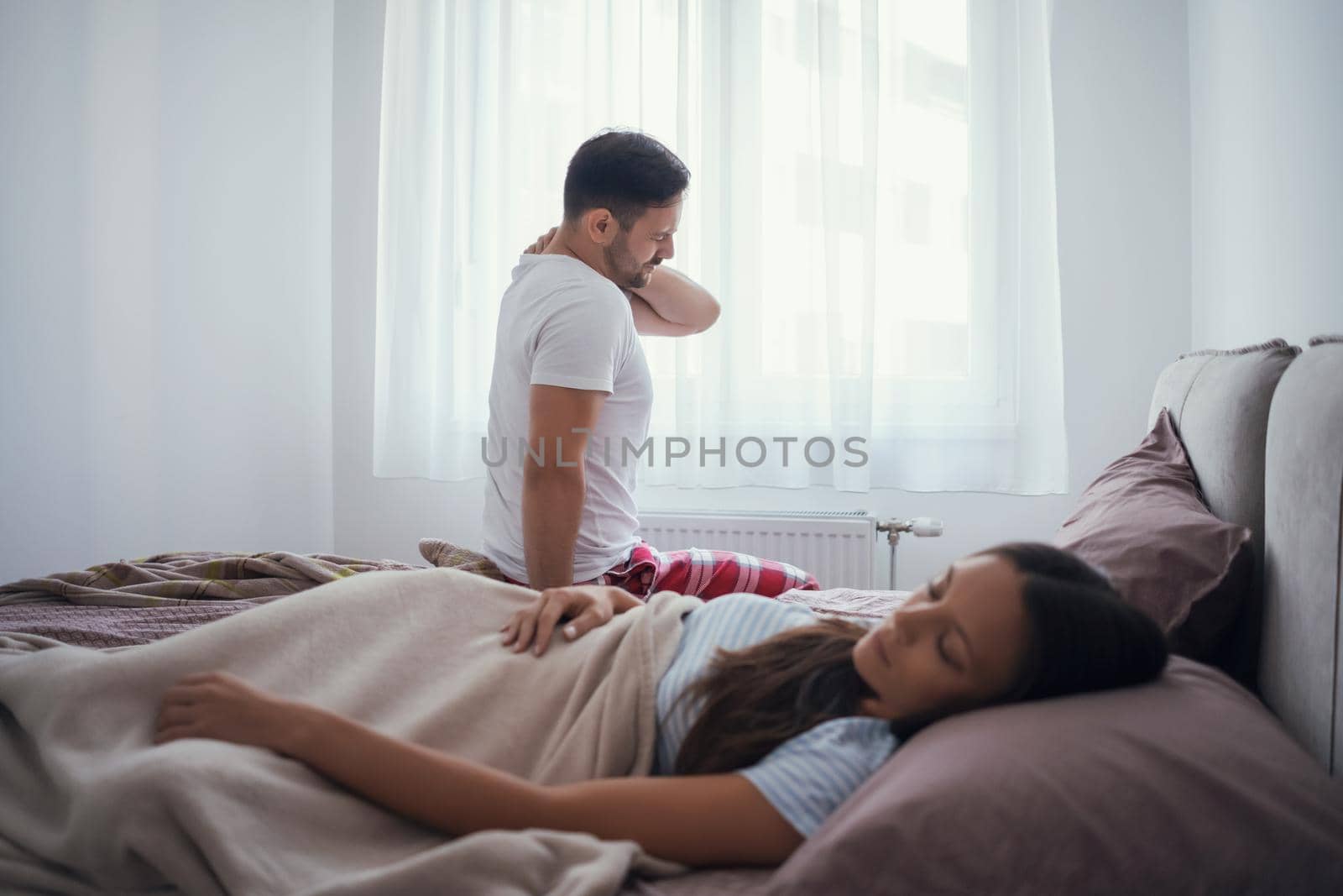 Young couple is waking up in the morning. Man has pain in neck.