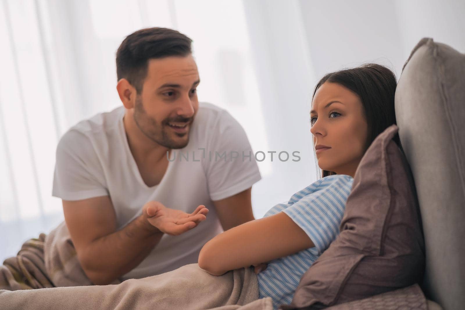 Young couple is arguing in bed. Woman is offended and angry.