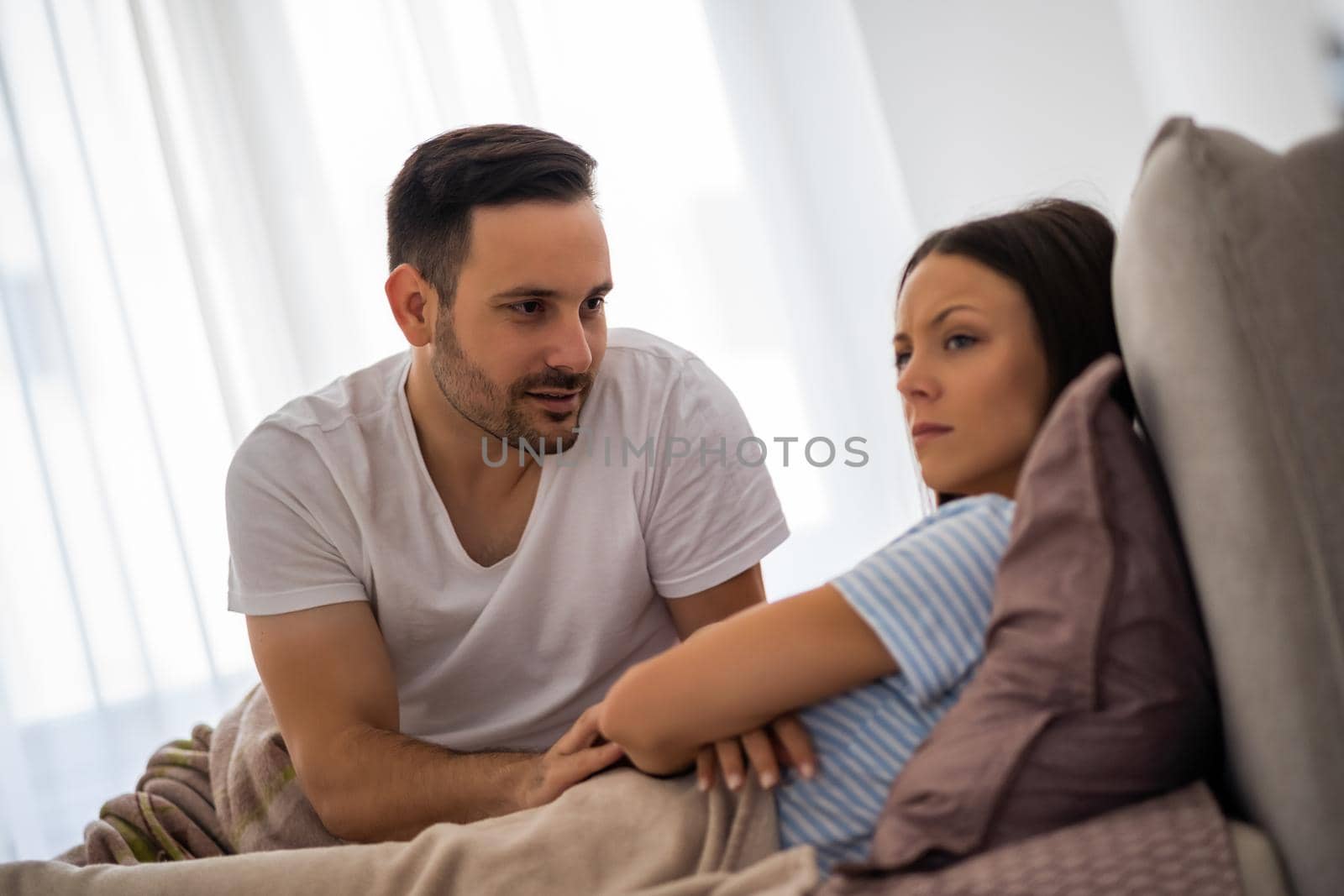 Young couple is arguing in bed. Woman is offended and angry.