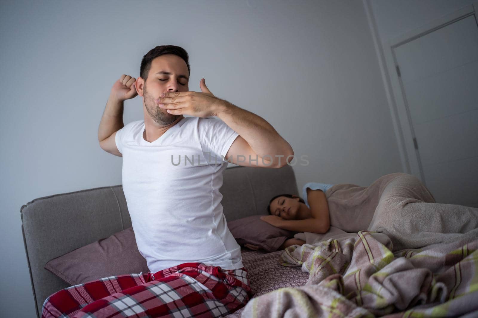 Young couple is sleeping in bed. Man is waking up for work.