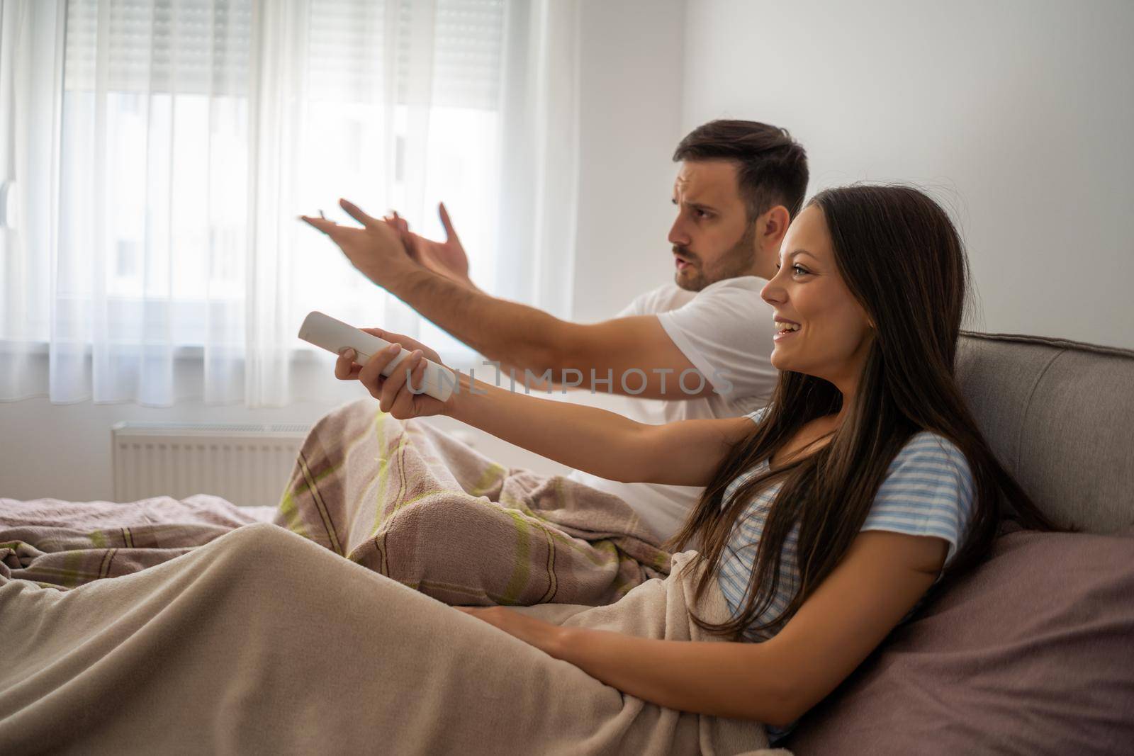 Young couple is watching tv in their bedroom.