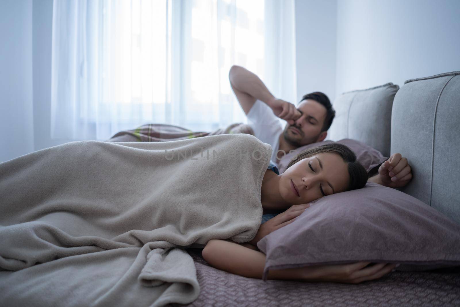 Young couple is sleeping in bed. Man is waking up for work.