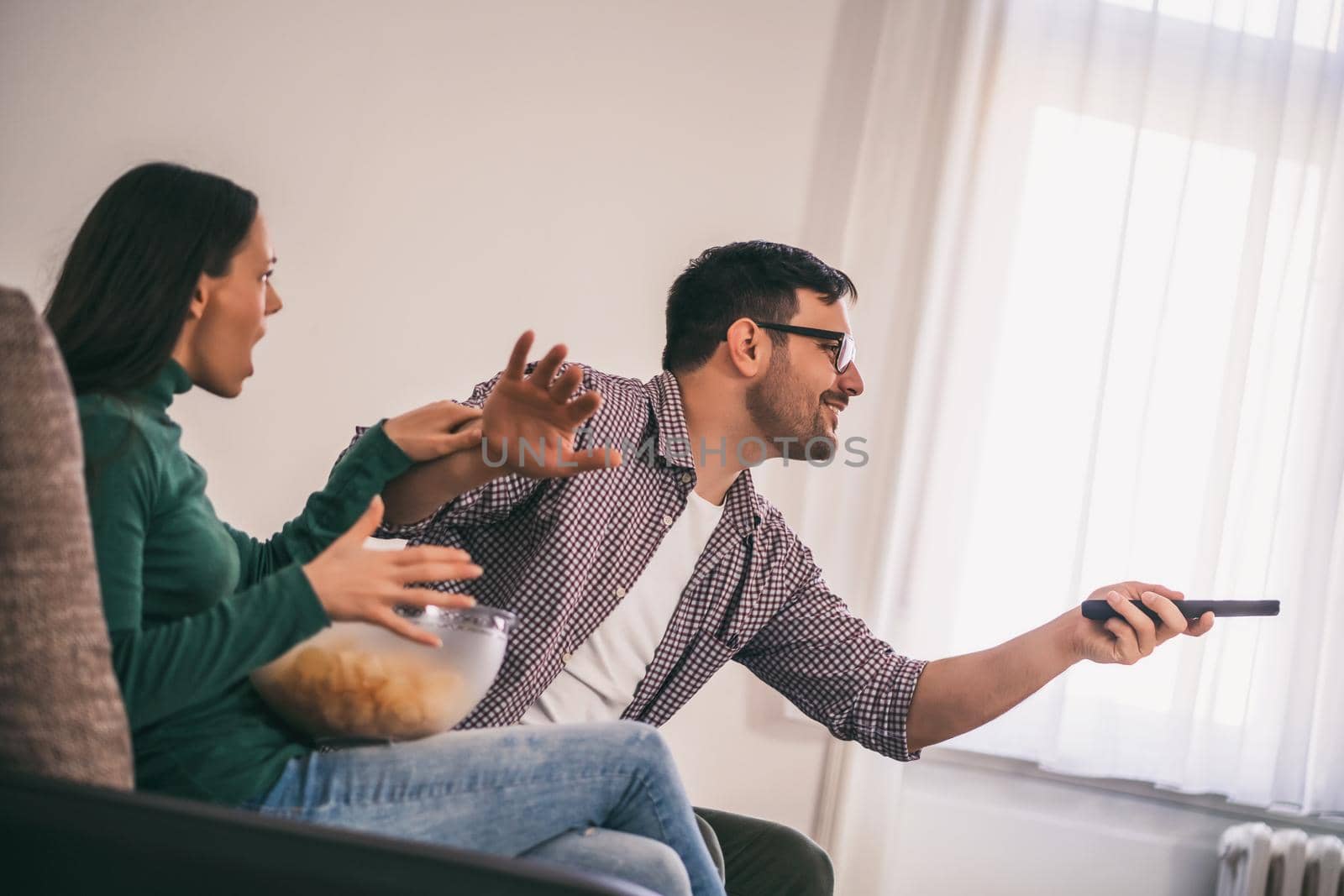 Young couple is watching tv at home. They are arguing.