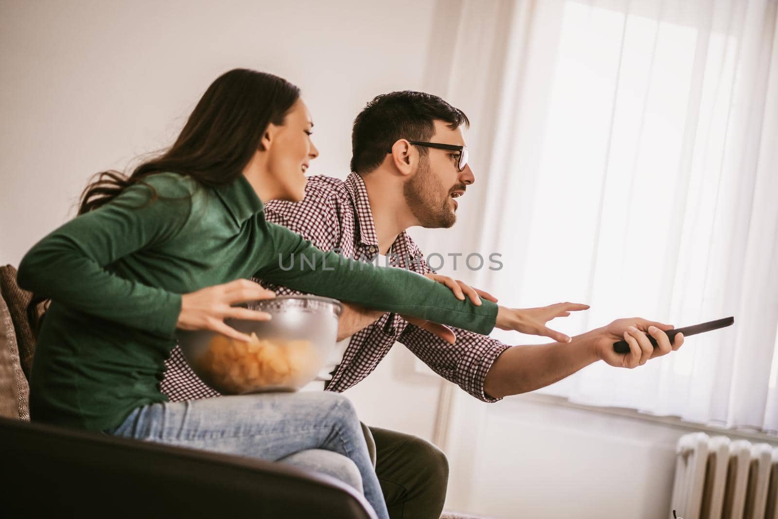 Young couple is watching tv at home. They are arguing.