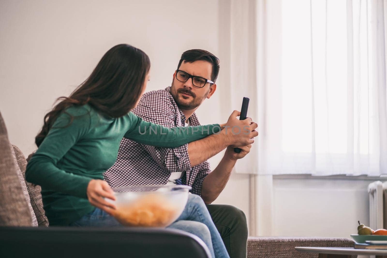 Young couple is watching tv at home. They are arguing.