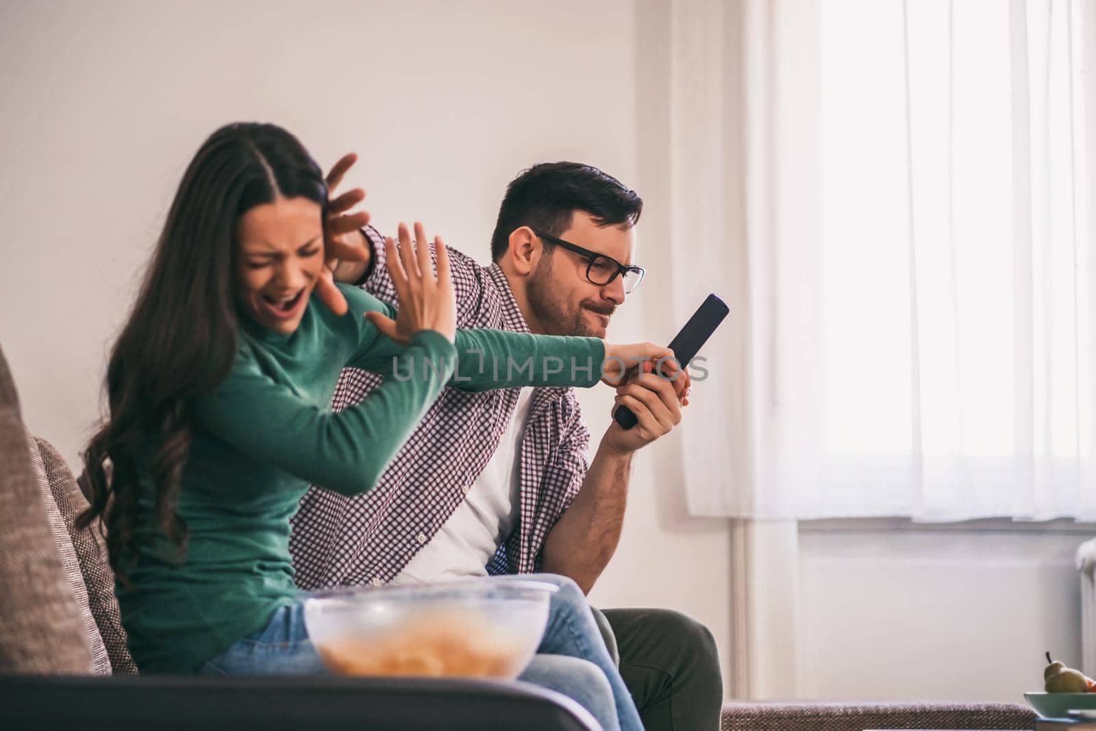 Young couple is watching tv at home. They are arguing.