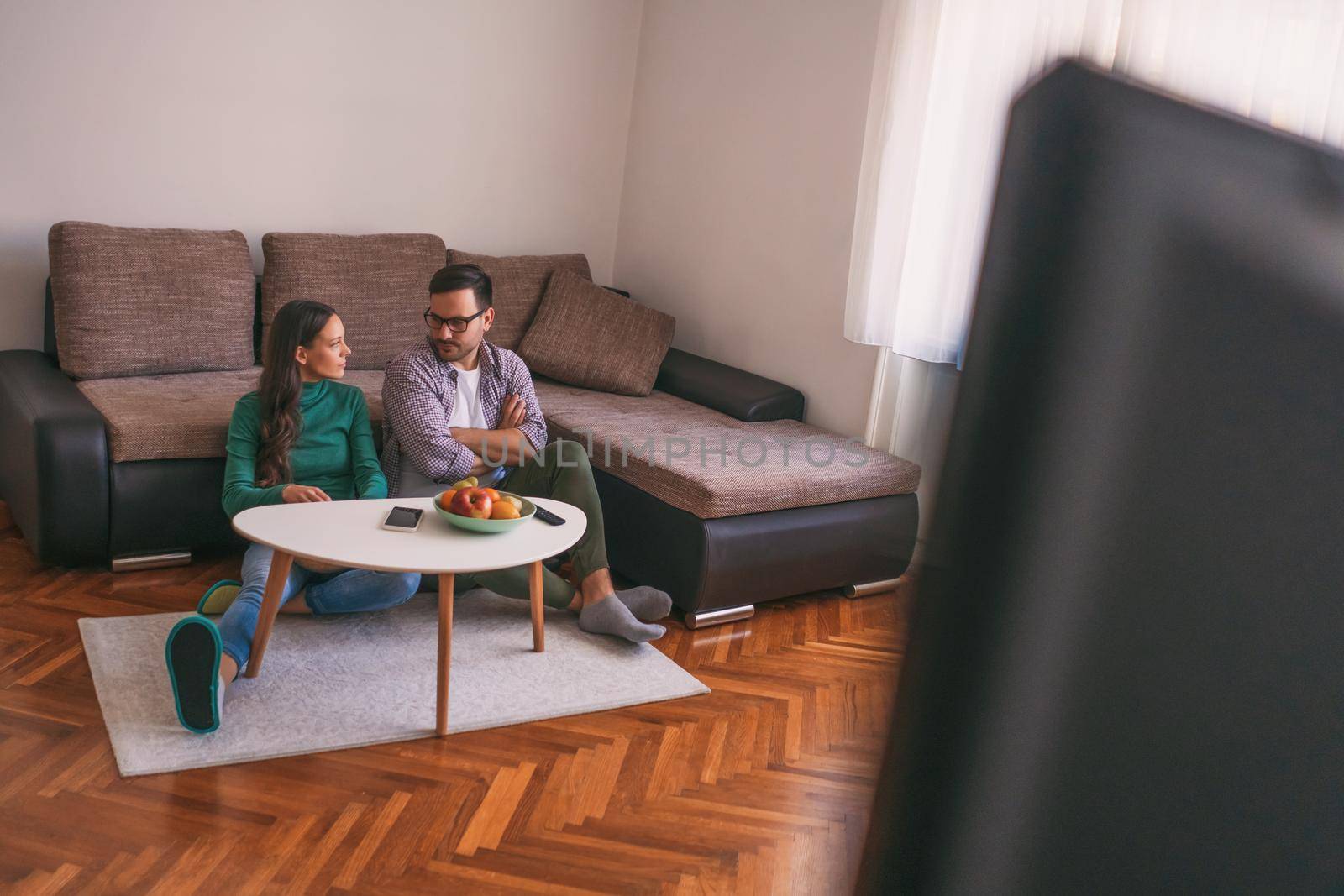 Young couple is watching tv at home. Man is not satisfied with tv program.