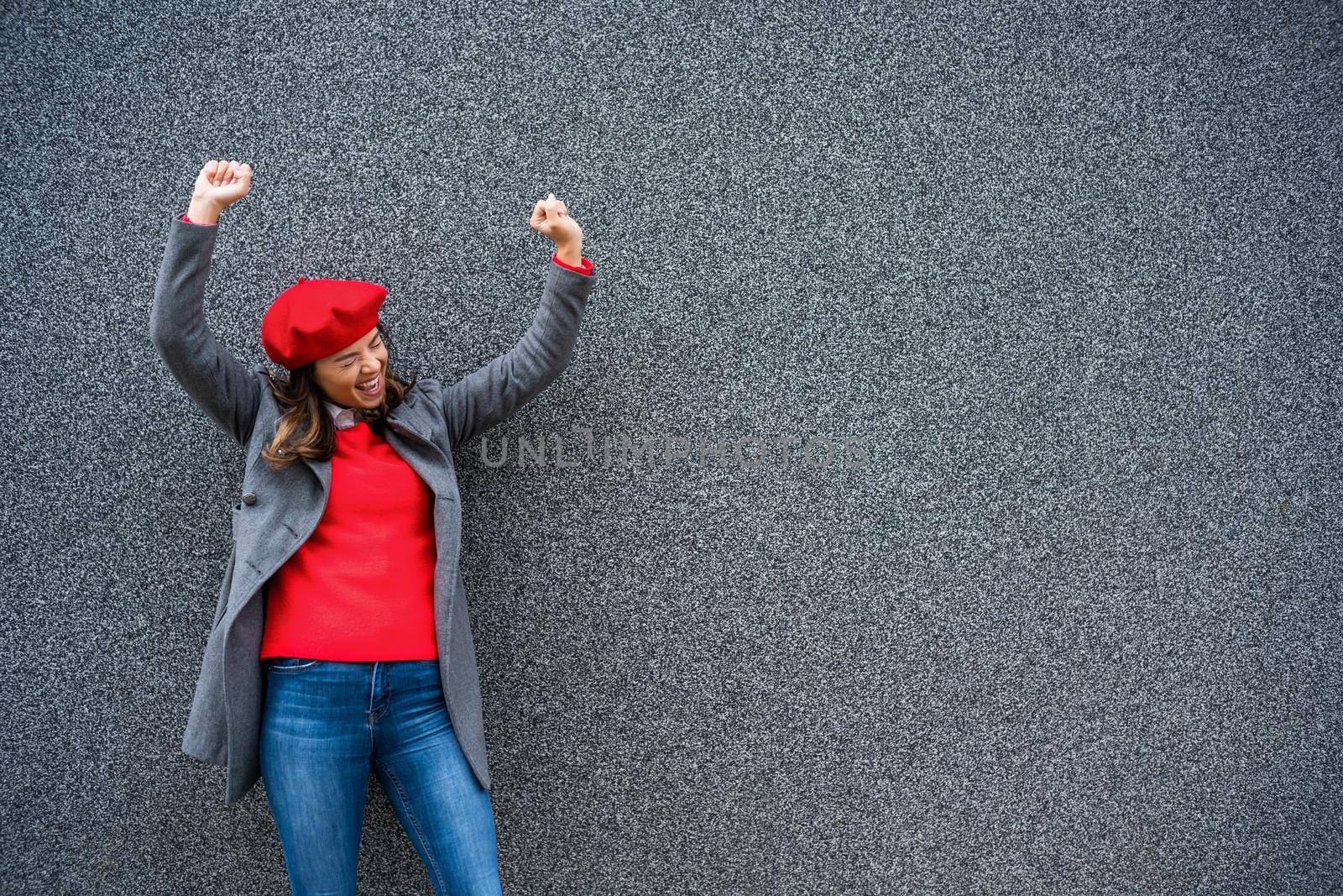 Adult woman in modern casual clothing standing in front of gray background. She is ecstatic. Copy space for your advert.