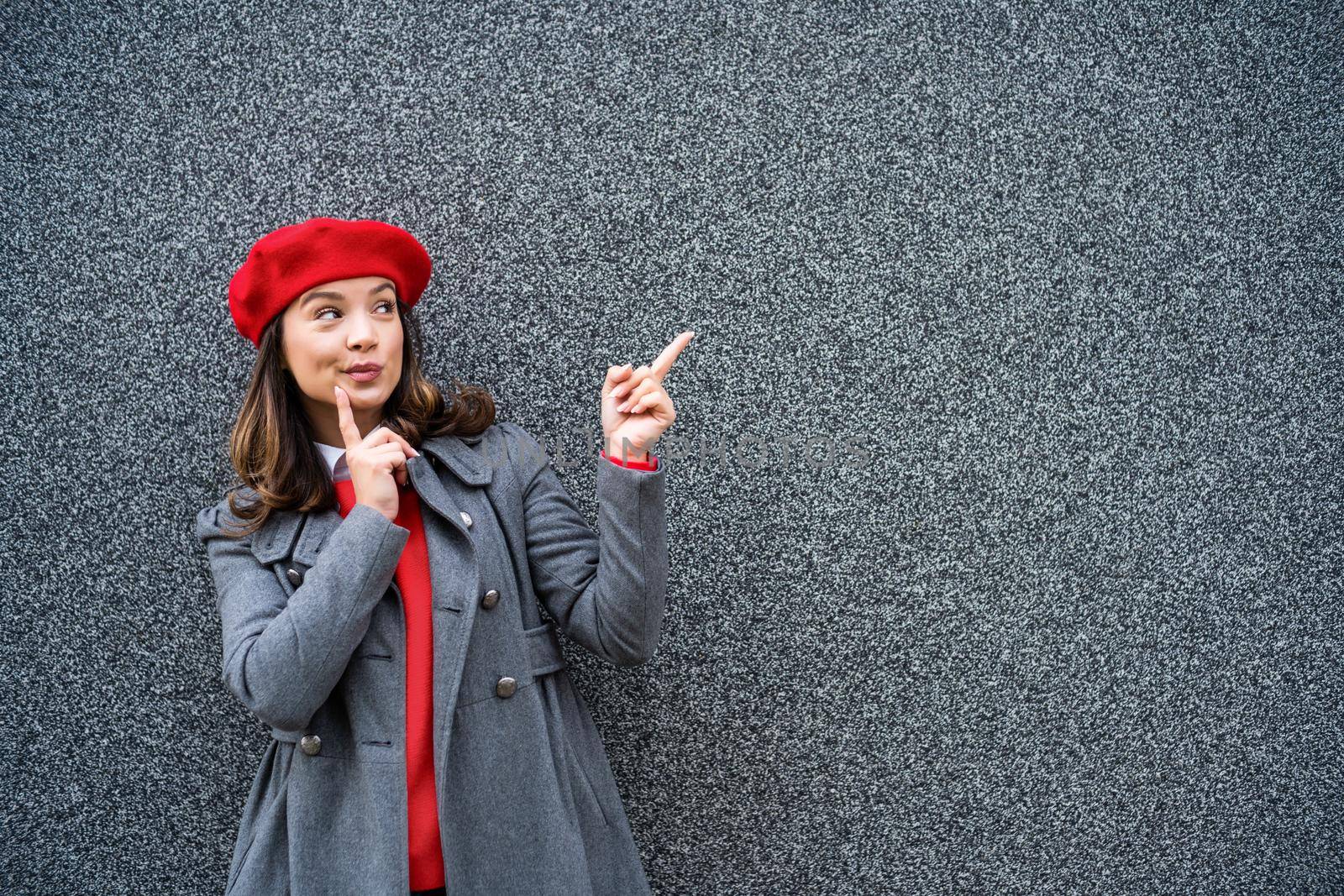 Adult woman in modern casual clothing standing in front of gray background. She is pointing at copy space for your advert.