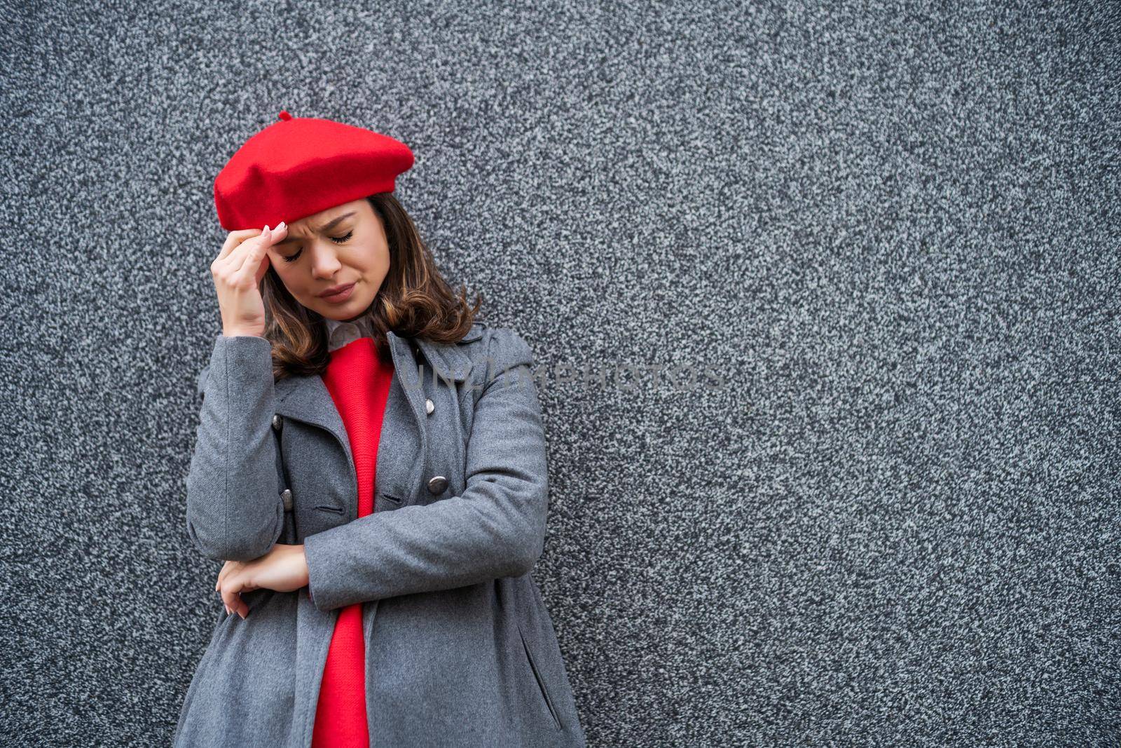 Adult woman in modern casual clothing standing in front of gray background. She is depressed. Copy space for your advert.