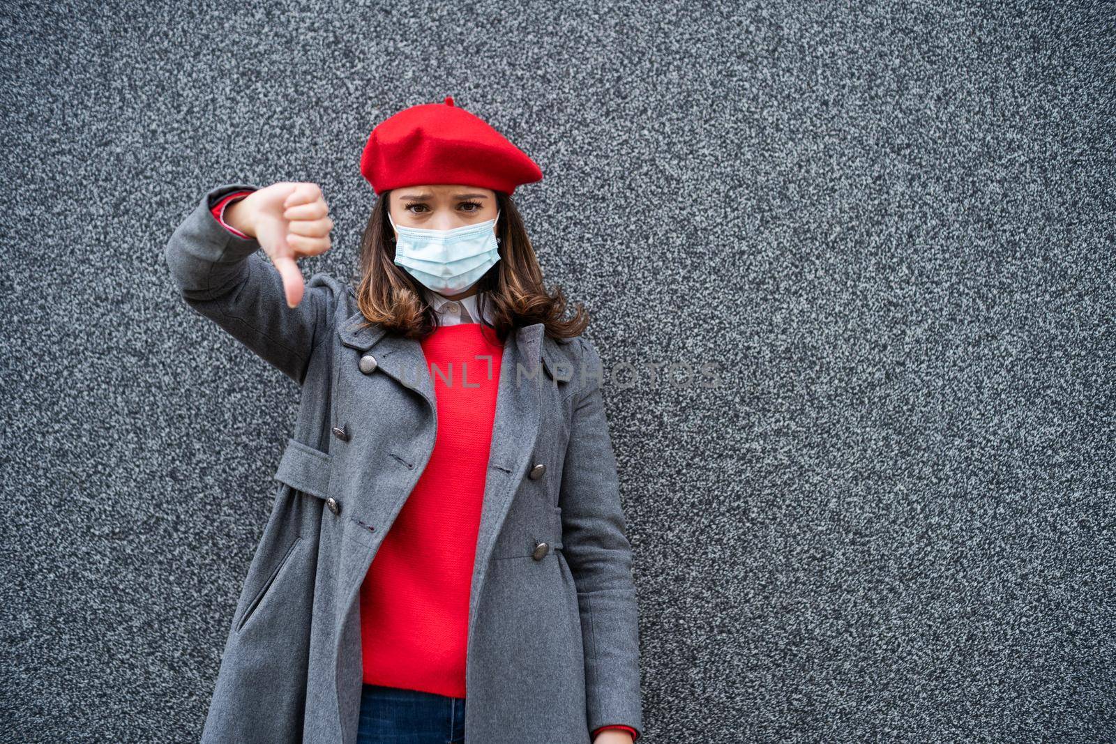 Adult woman in modern casual clothing standing in front of gray background. She is wearing protective mask. Copy space for your advert.