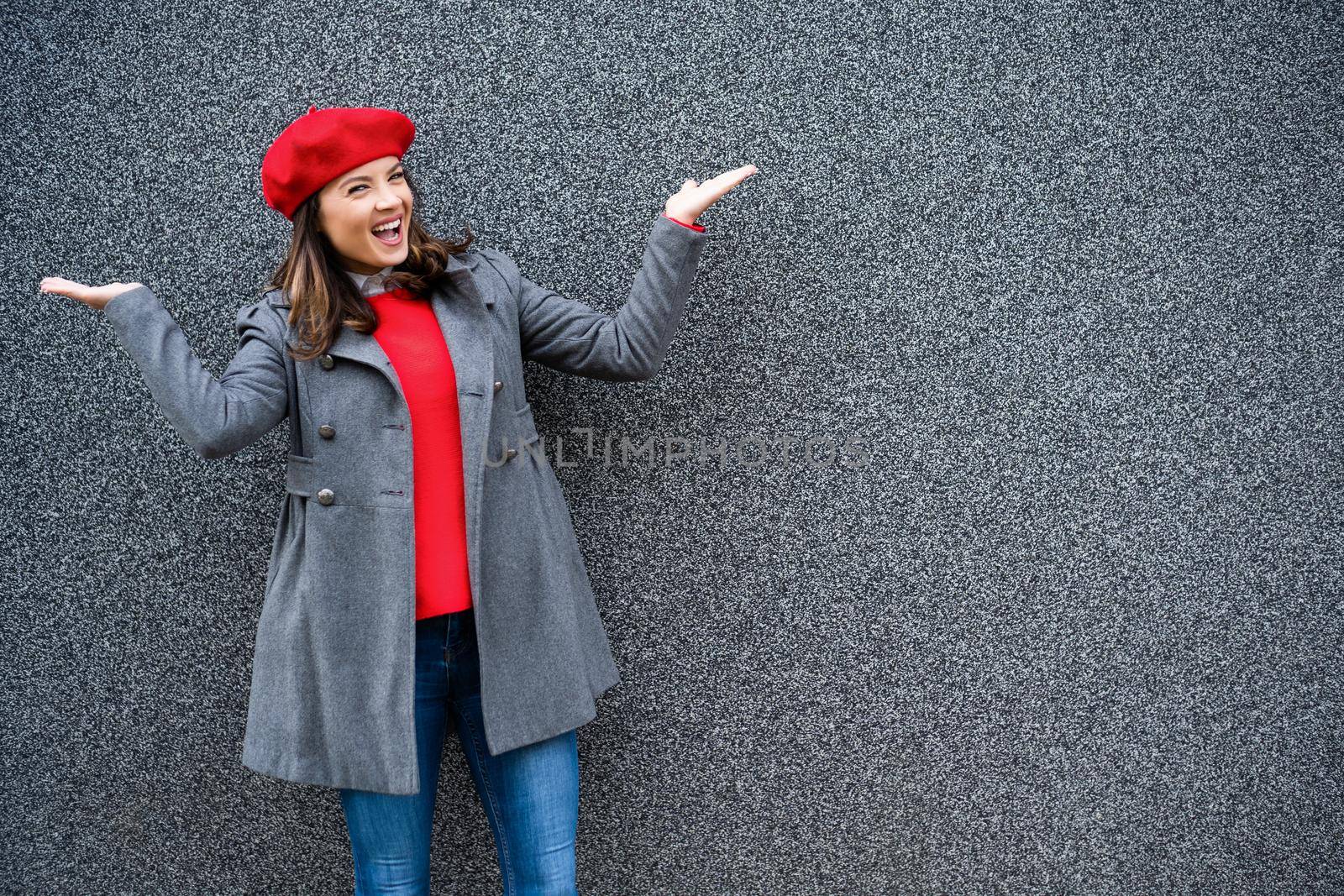 Adult woman in modern casual clothing standing in front of gray background. She is cheerful and looking at camera. Copy space for your advert.