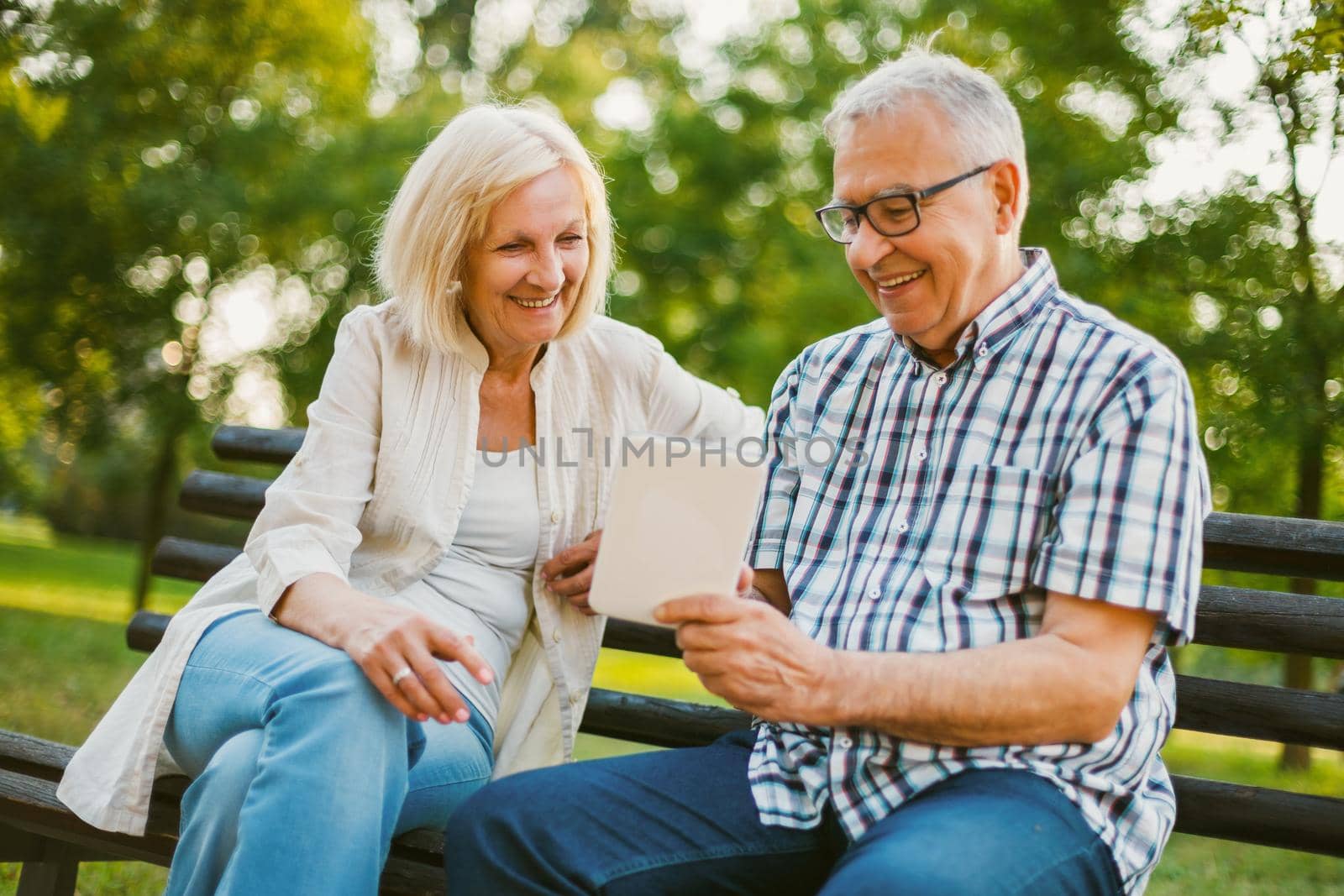 Happy senior couple is using digital tablet in park.