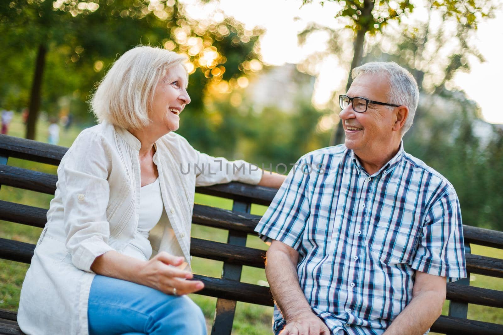 Two happy seniors are sitting and talking in park.