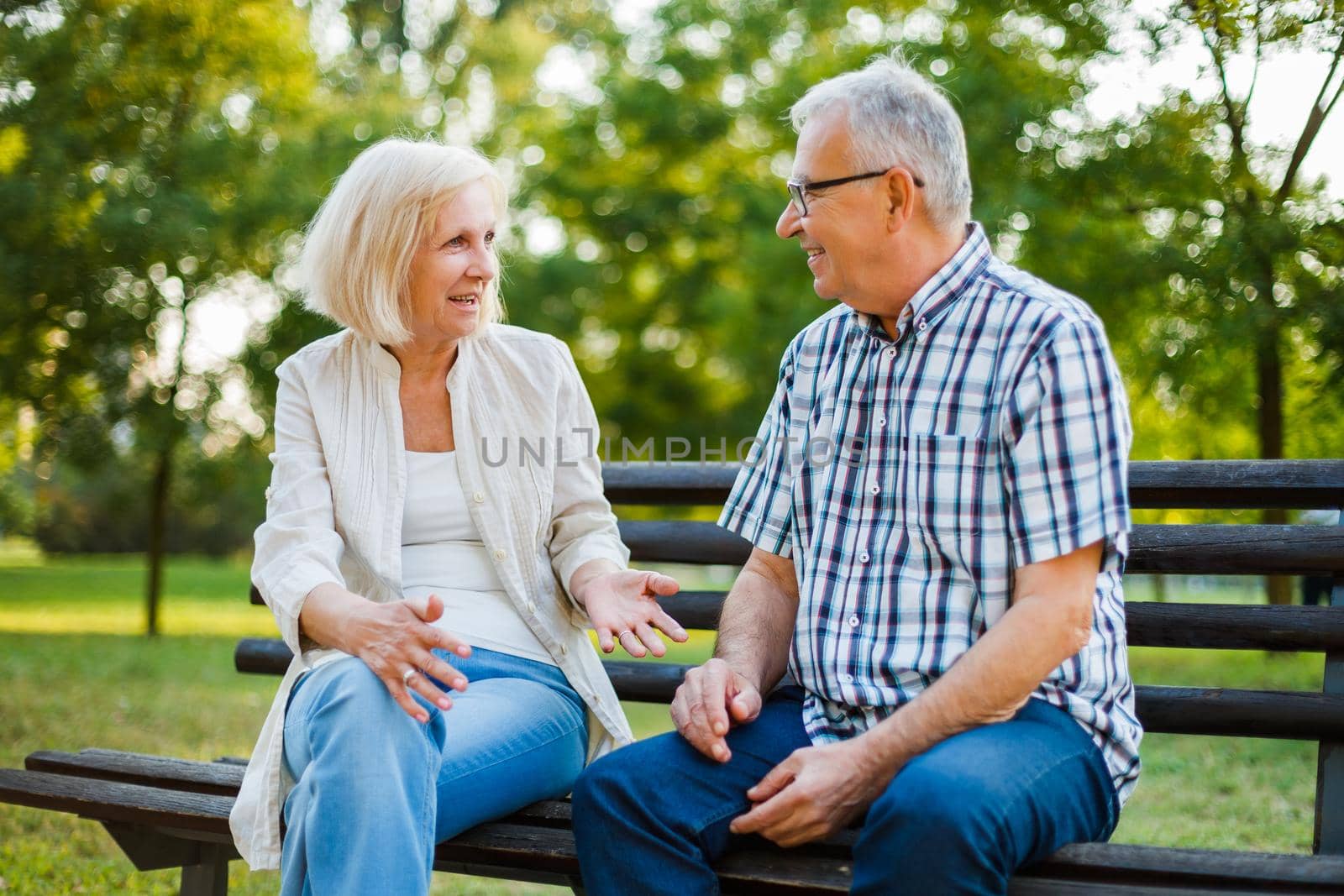 Two happy seniors are sitting and talking in park.