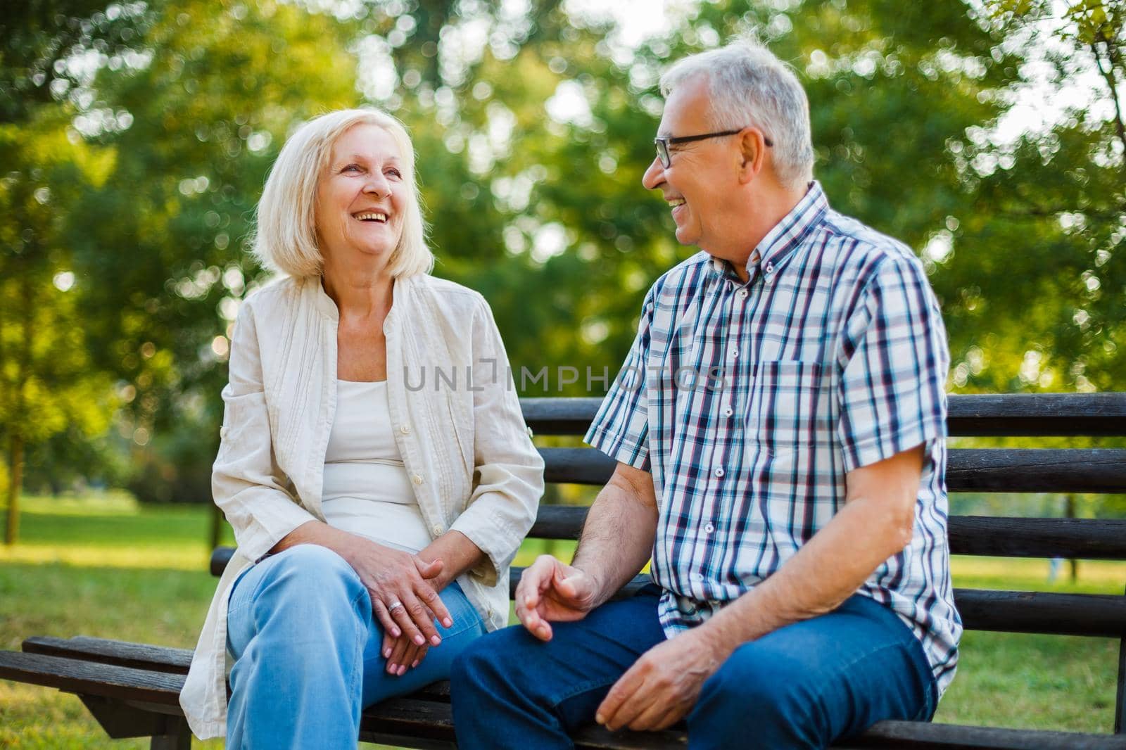 Two happy seniors are sitting and talking in park.