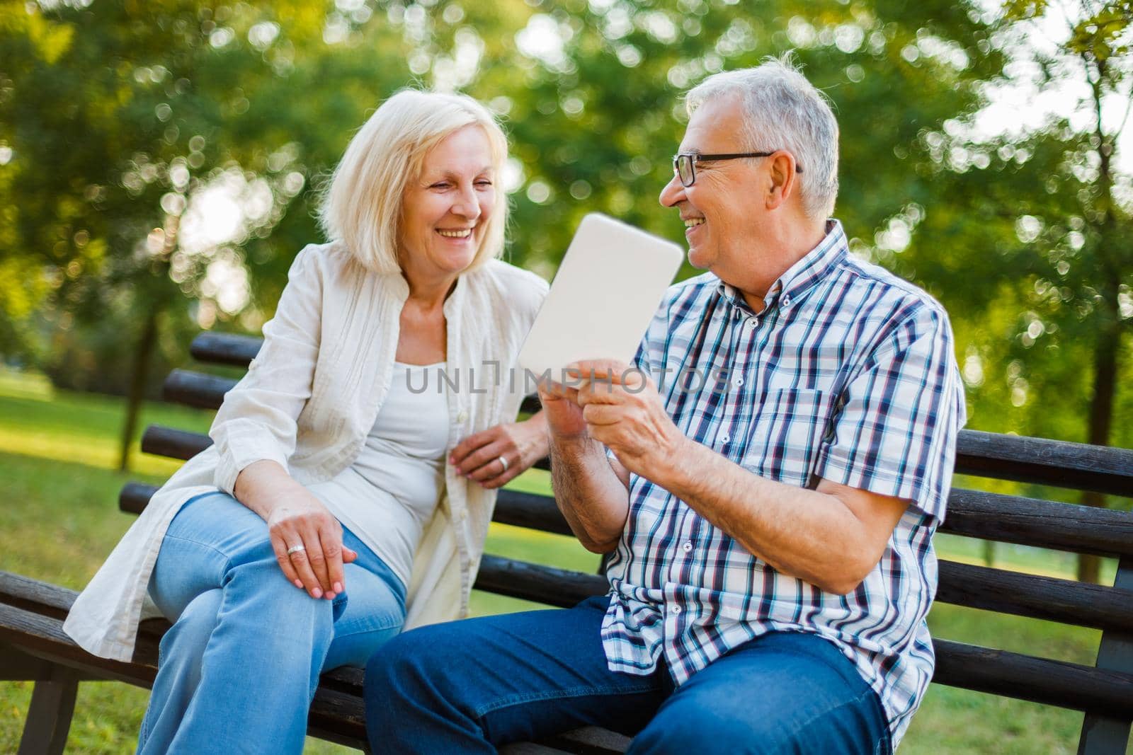 Happy senior couple is using digital tablet in park.