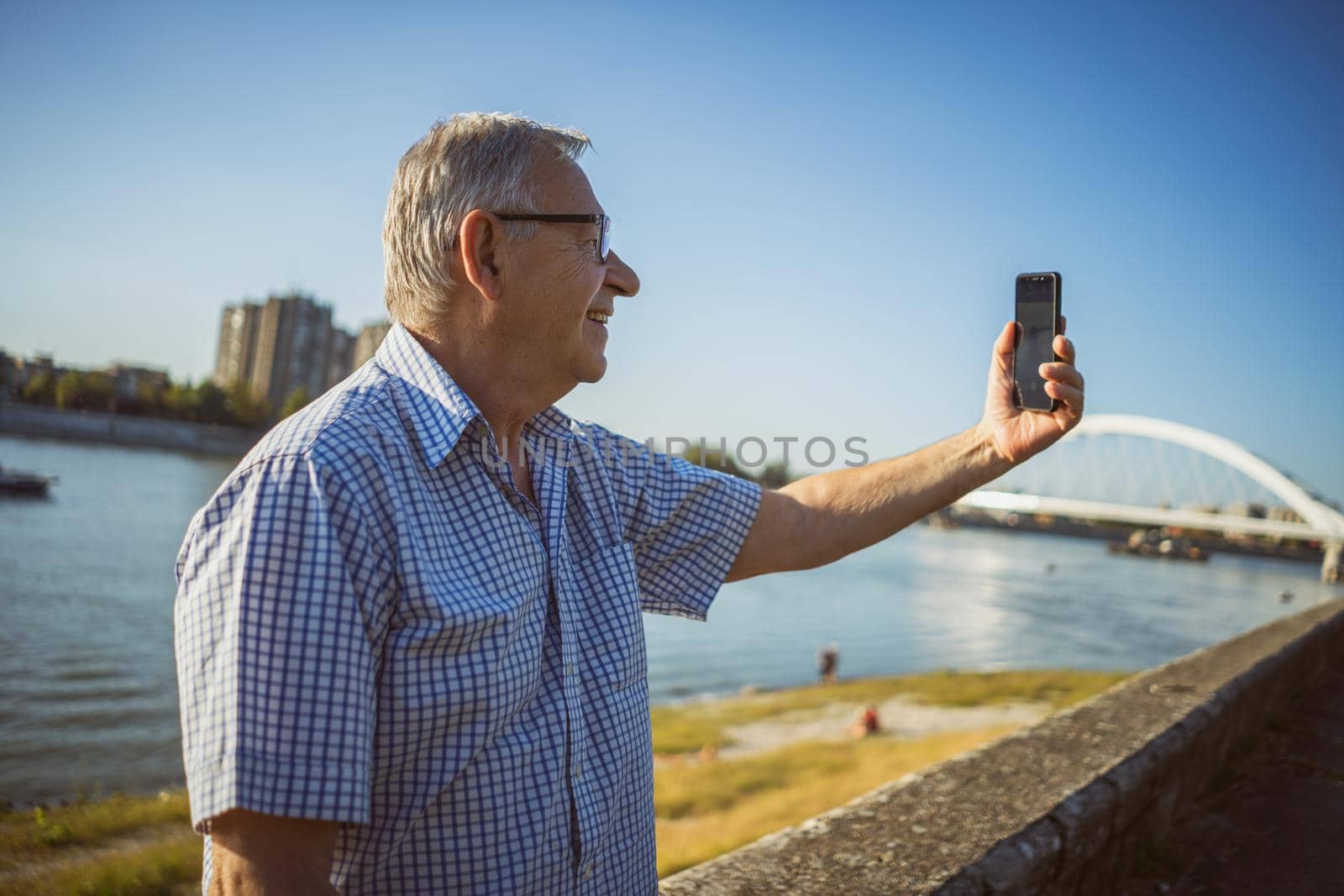 Outdoor portrait of senior man who is taking selfie.