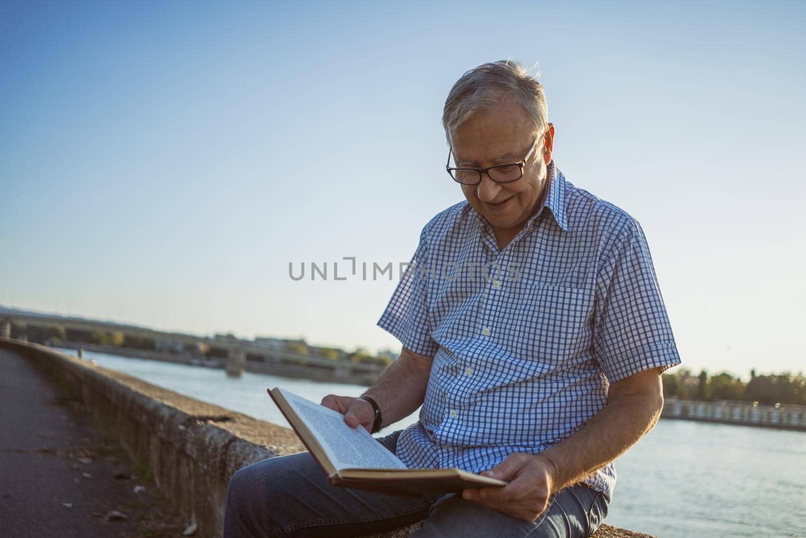 Outdoor portrait of senior man who is reading book.