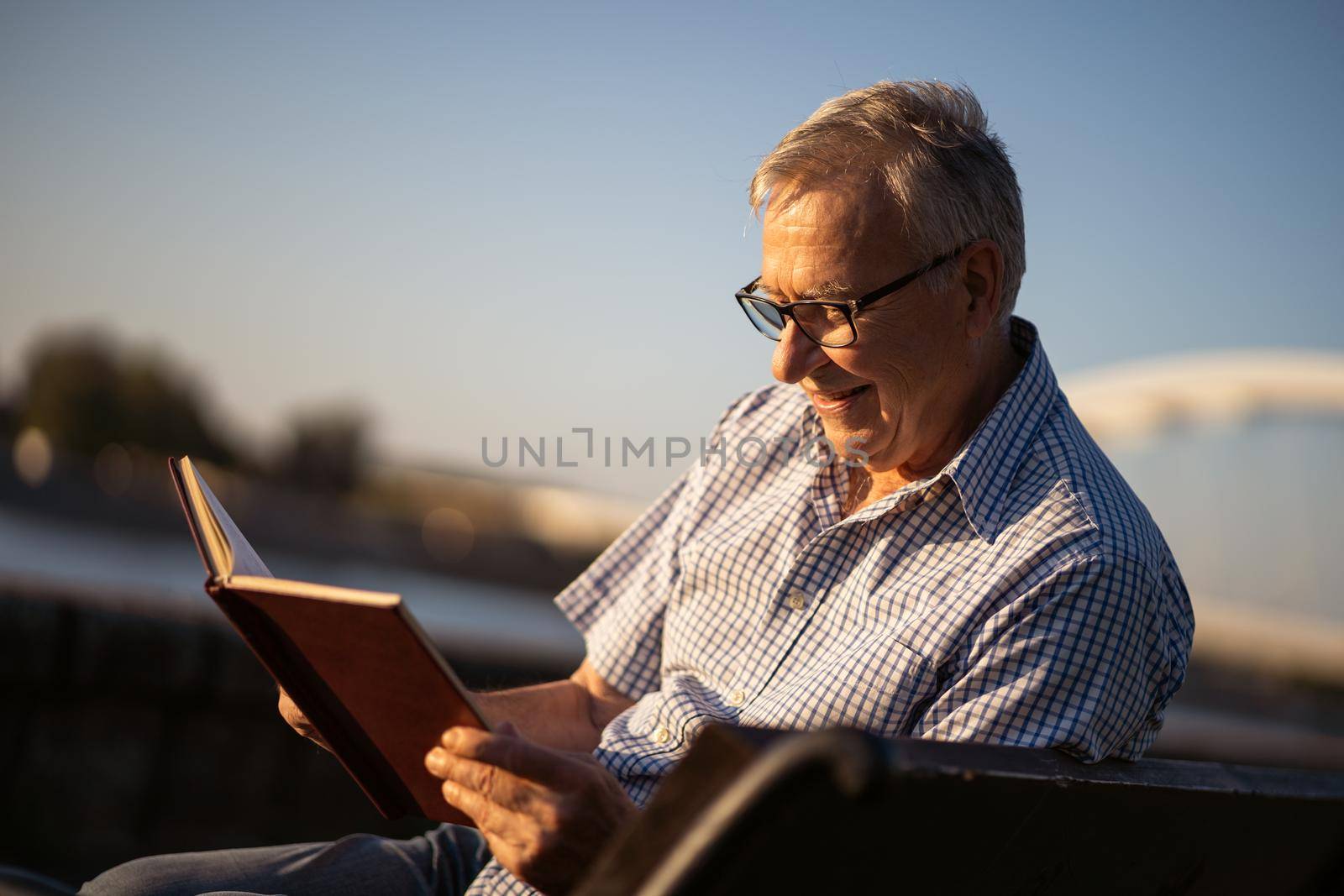 Outdoor portrait of senior man who is reading a book.