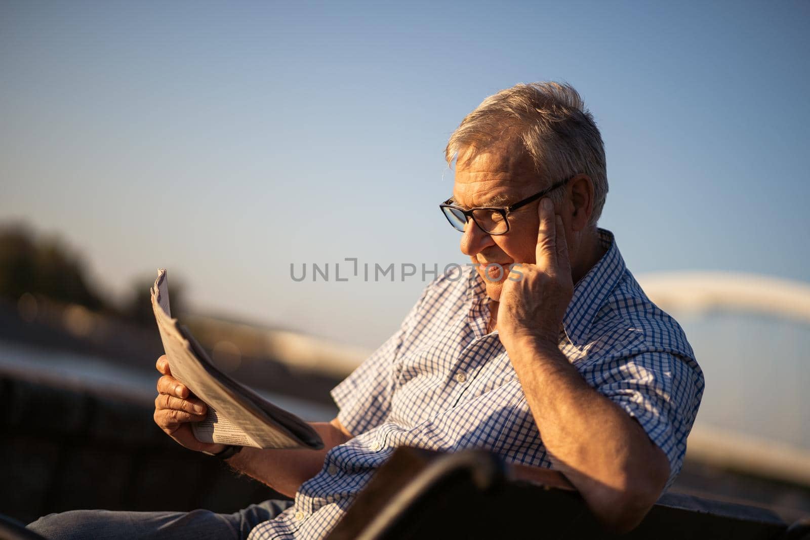 Outdoor portrait of senior man who is reading newspapers.