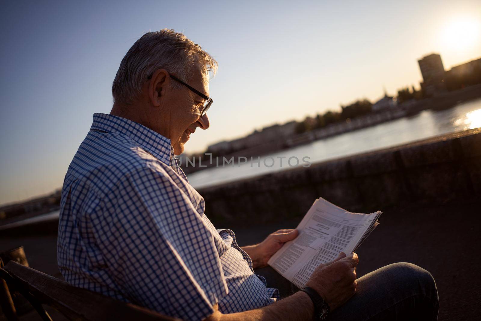 Outdoor portrait of senior man who is reading newspapers.