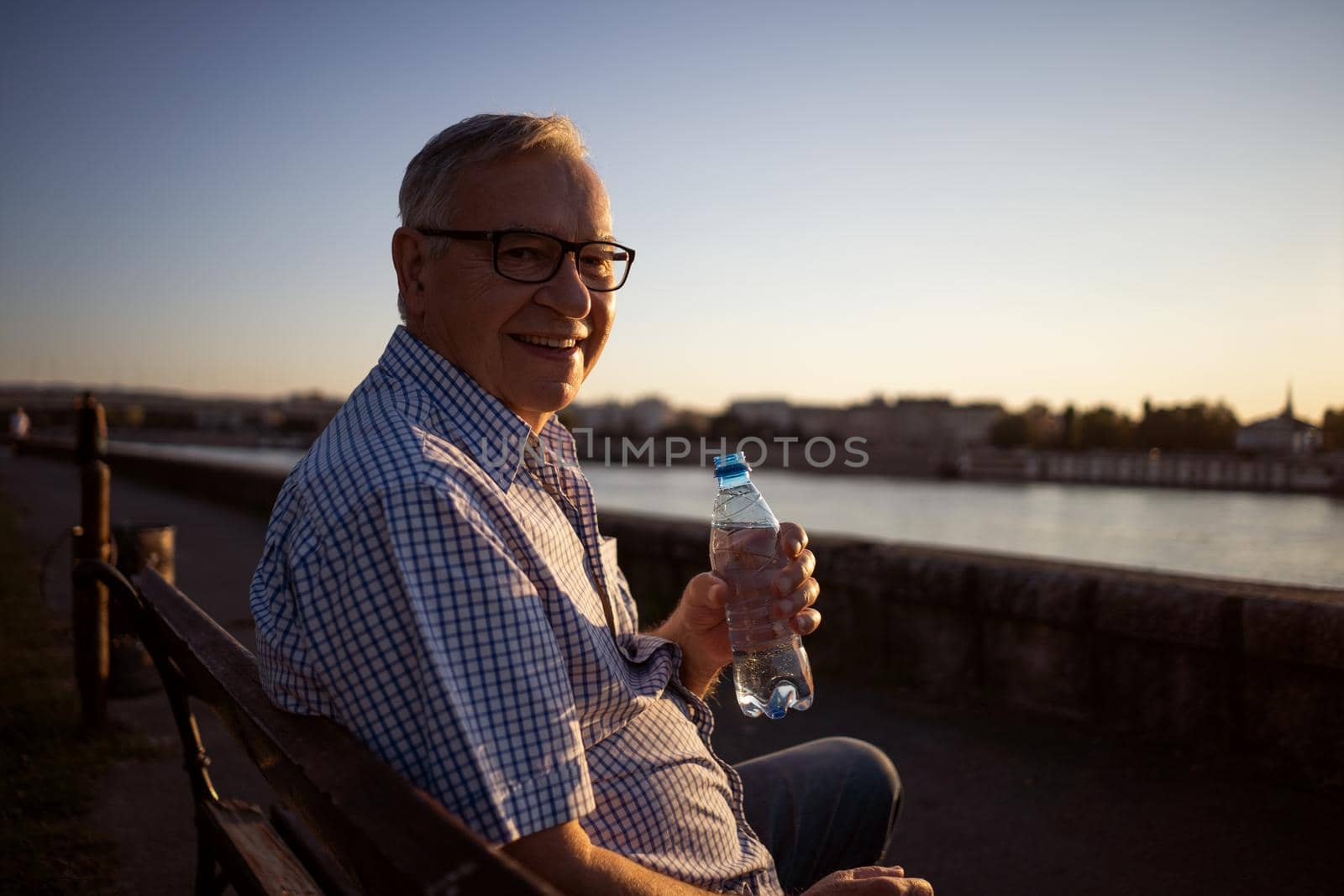 Outdoor portrait of senior man who is holding bottle of water.