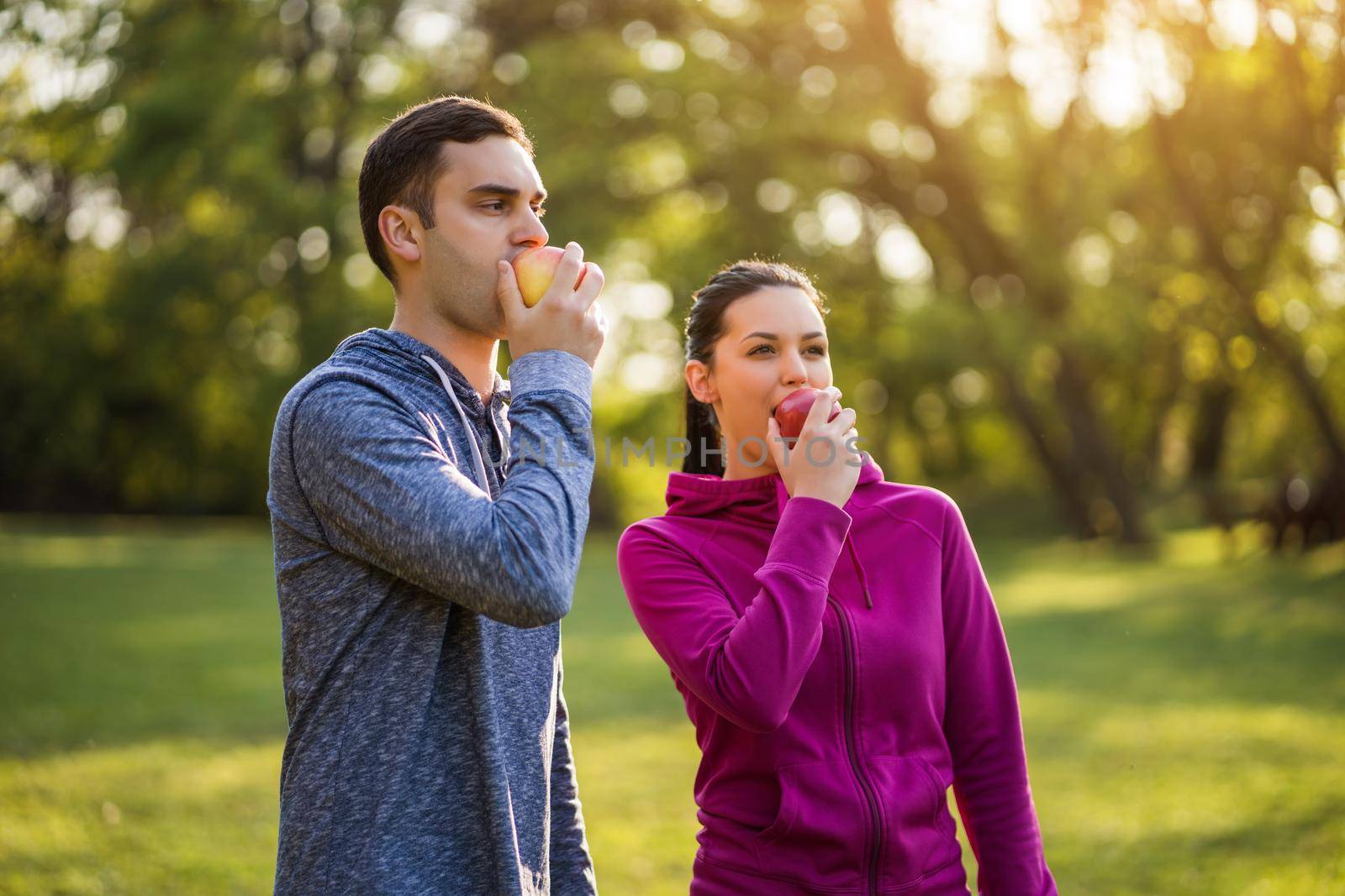 Young couple is eating apple after exercising in park.