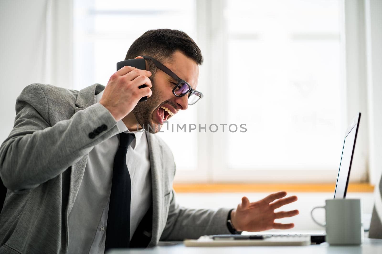 Furious businessman is talking on phone in his office.