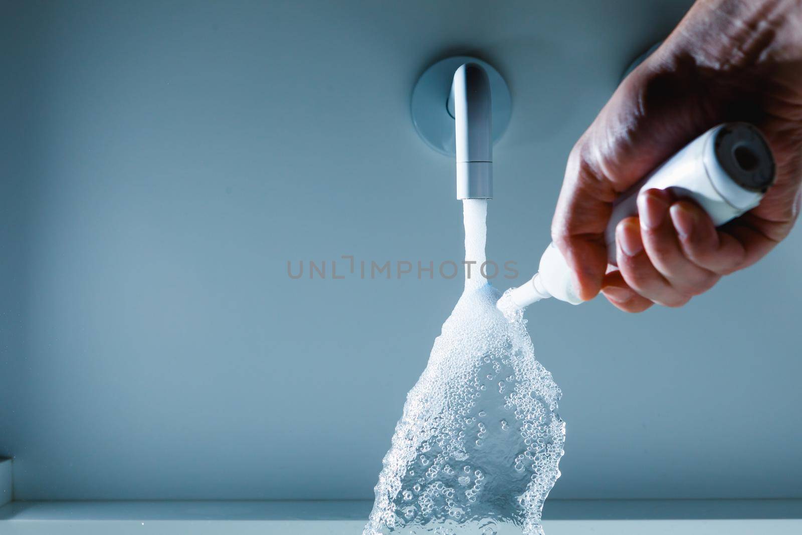 hand holding toothbrush under flowing water from faucet in a bathroom by nikkytok