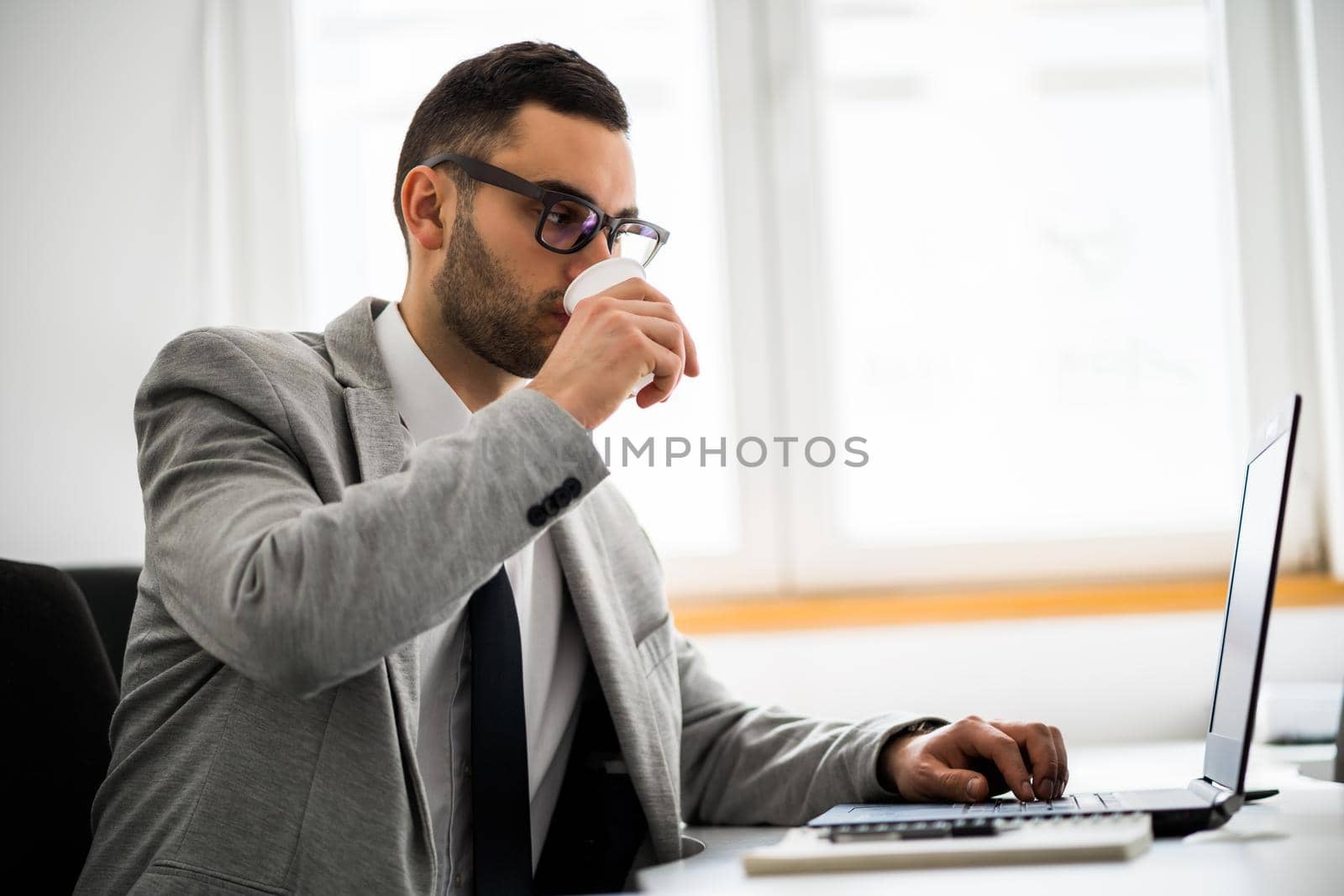 Young businessman is working in office. He is drinking coffee.