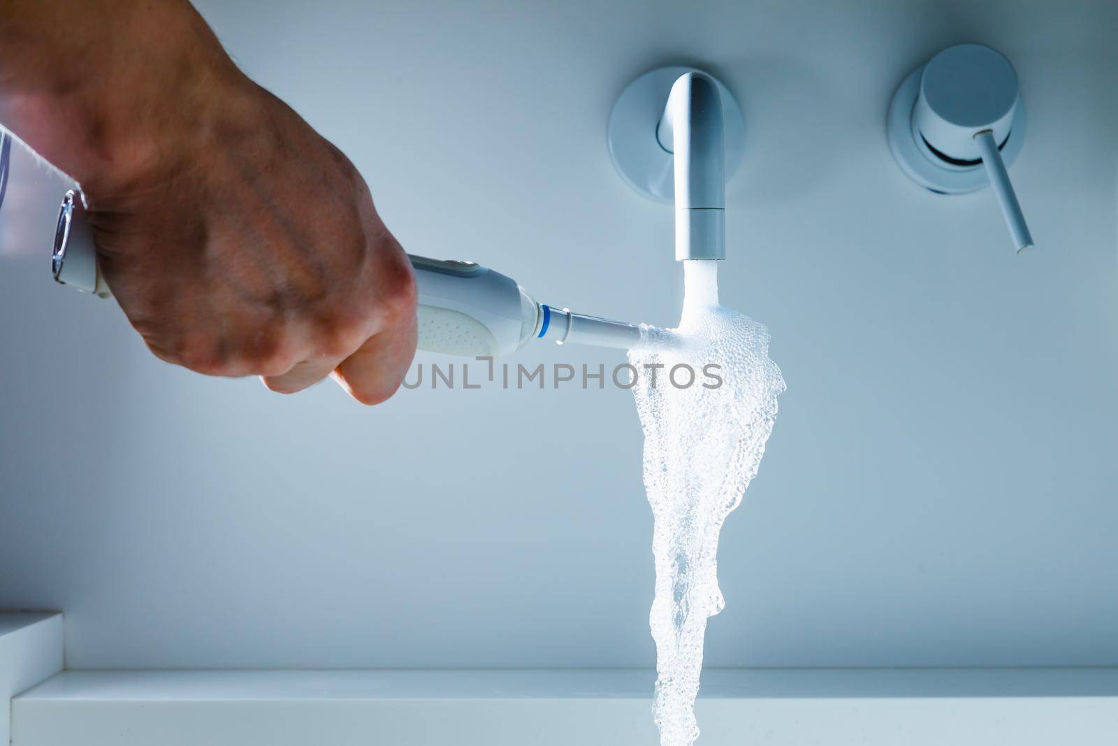 hand holding toothbrush under flowing water from faucet in a hospital by nikkytok