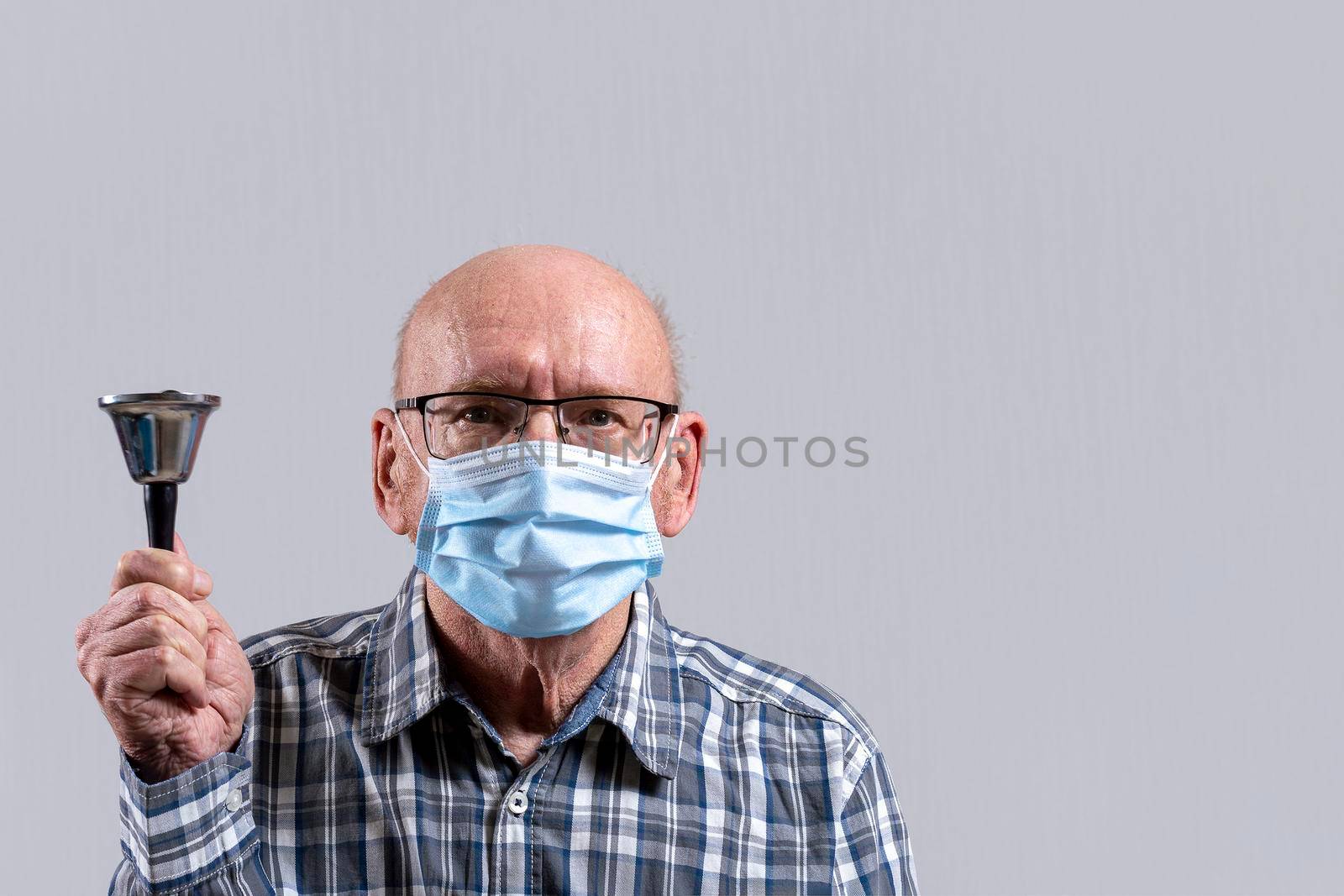 Old bald man with glasses and medical mask with bell in his hand. Copy space. by Essffes