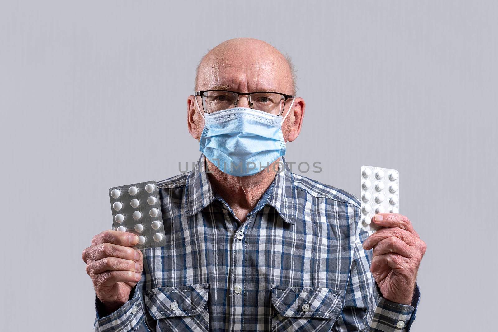 Old bald man with glasses and medical mask with pills in his hand. Copy space. by Essffes