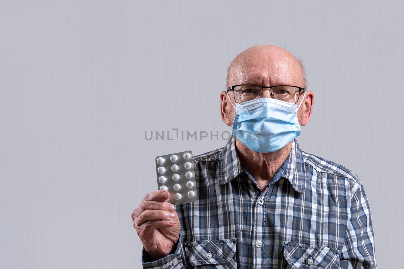 Old bald man with glasses and medical mask with pills in his hand. Copy space. by Essffes