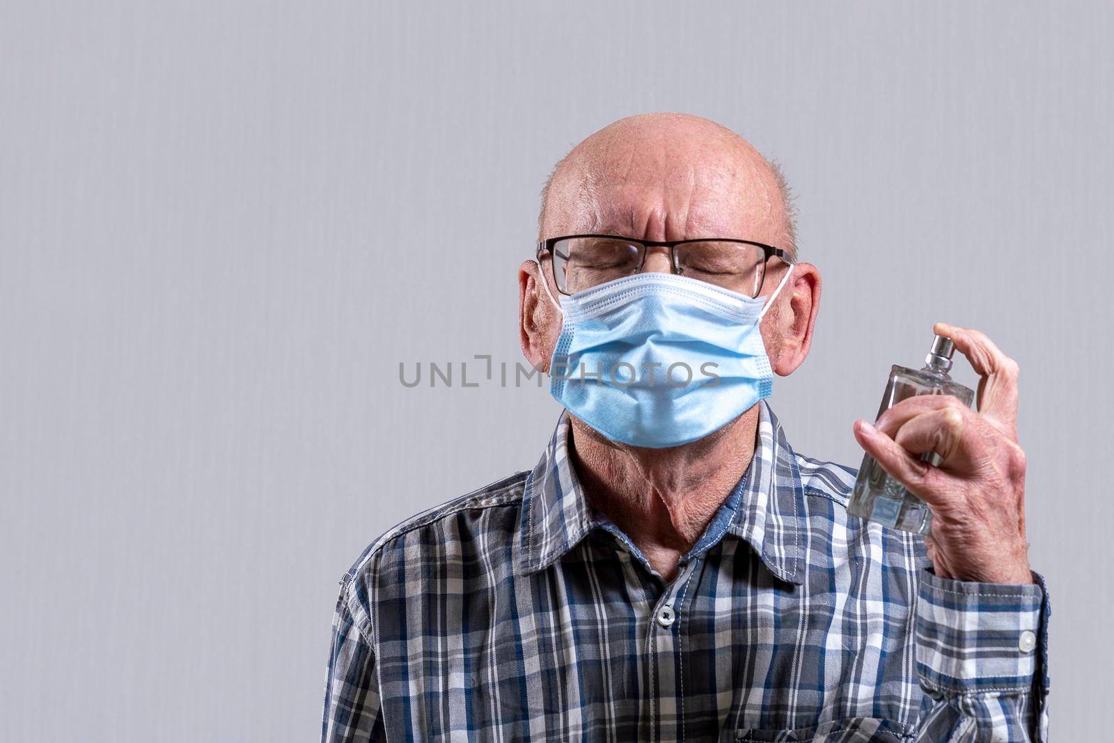 Old bald man with glasses and medical mask with perfume bottle spray in his hand. Copy space. by Essffes